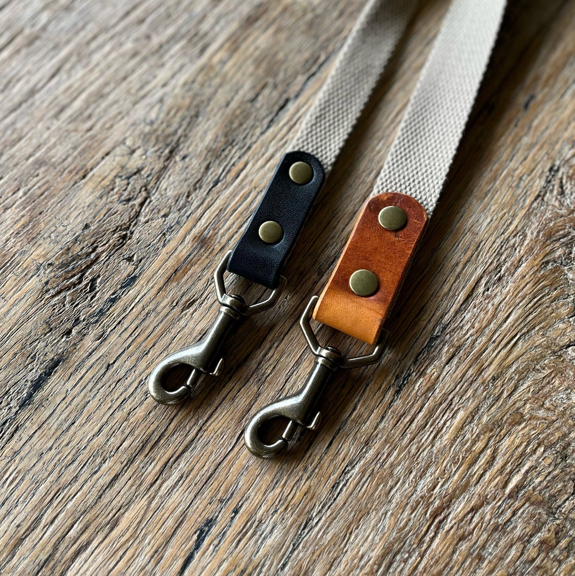Two leather dog lead snap clips on a wooden surface