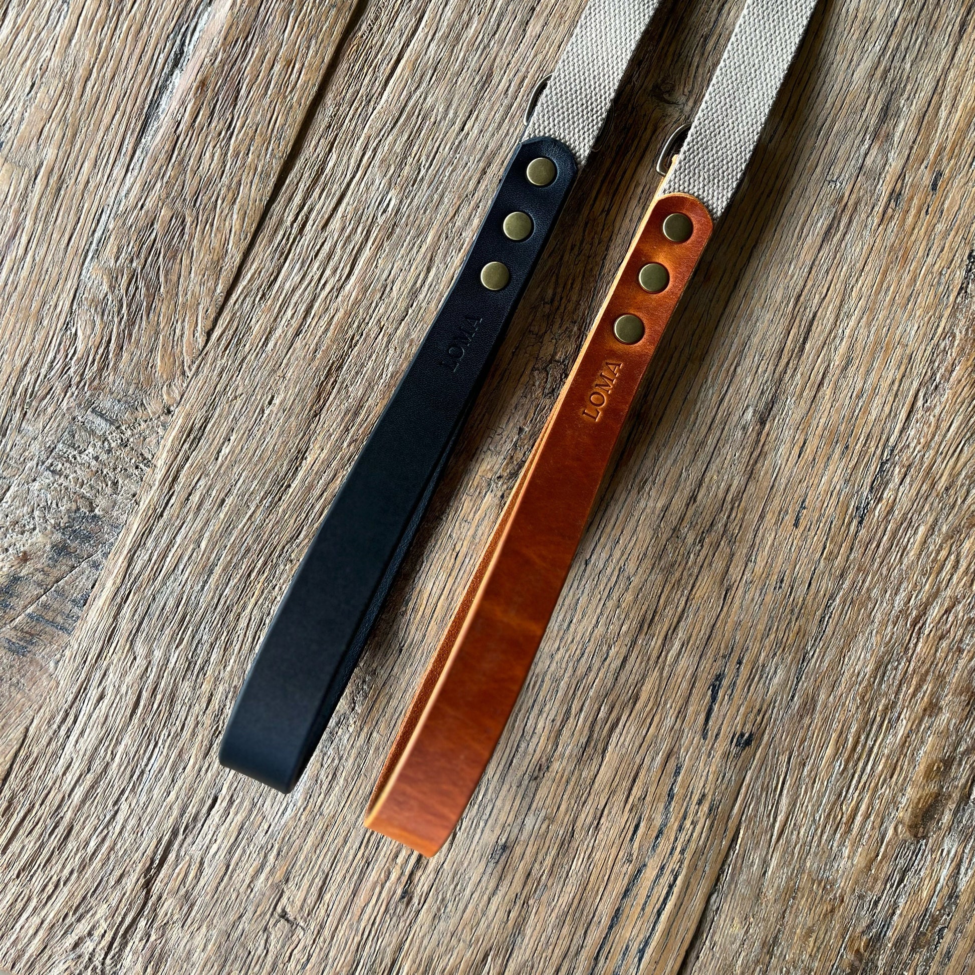 Two leather straps, one black and one brown, on a wooden surface.