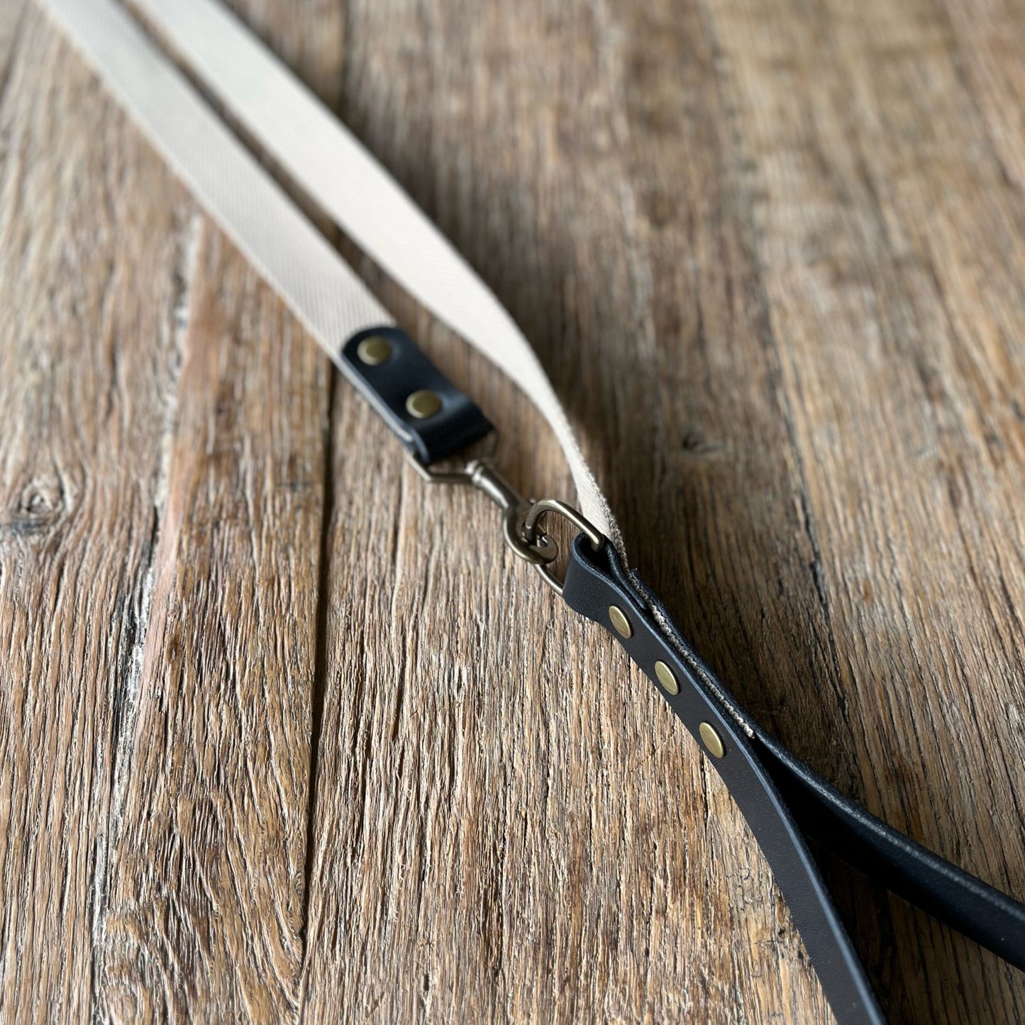 Close-up of a leather strap with brass hardware on a wooden surface