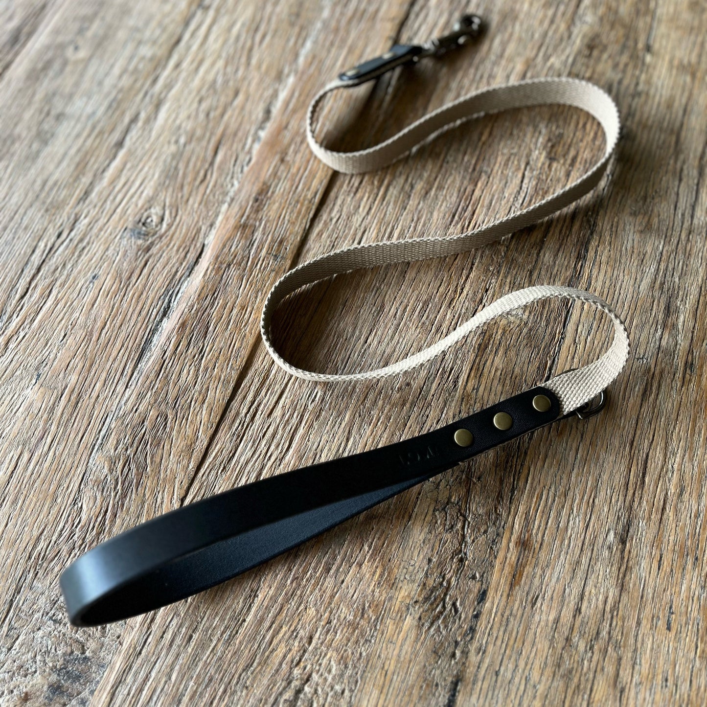 Leash with black leather end and beige fabric on a wooden surface