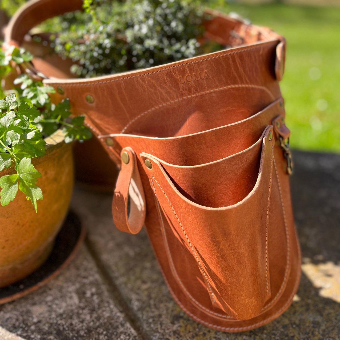 Brown leather tool pouch with plant pots in the background