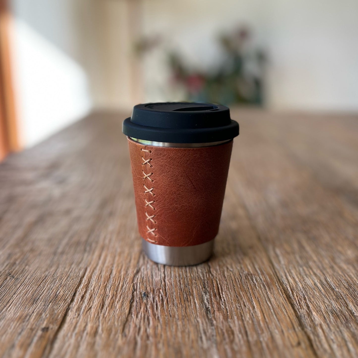 Brown leather coffee cup with black lid on a wooden surface