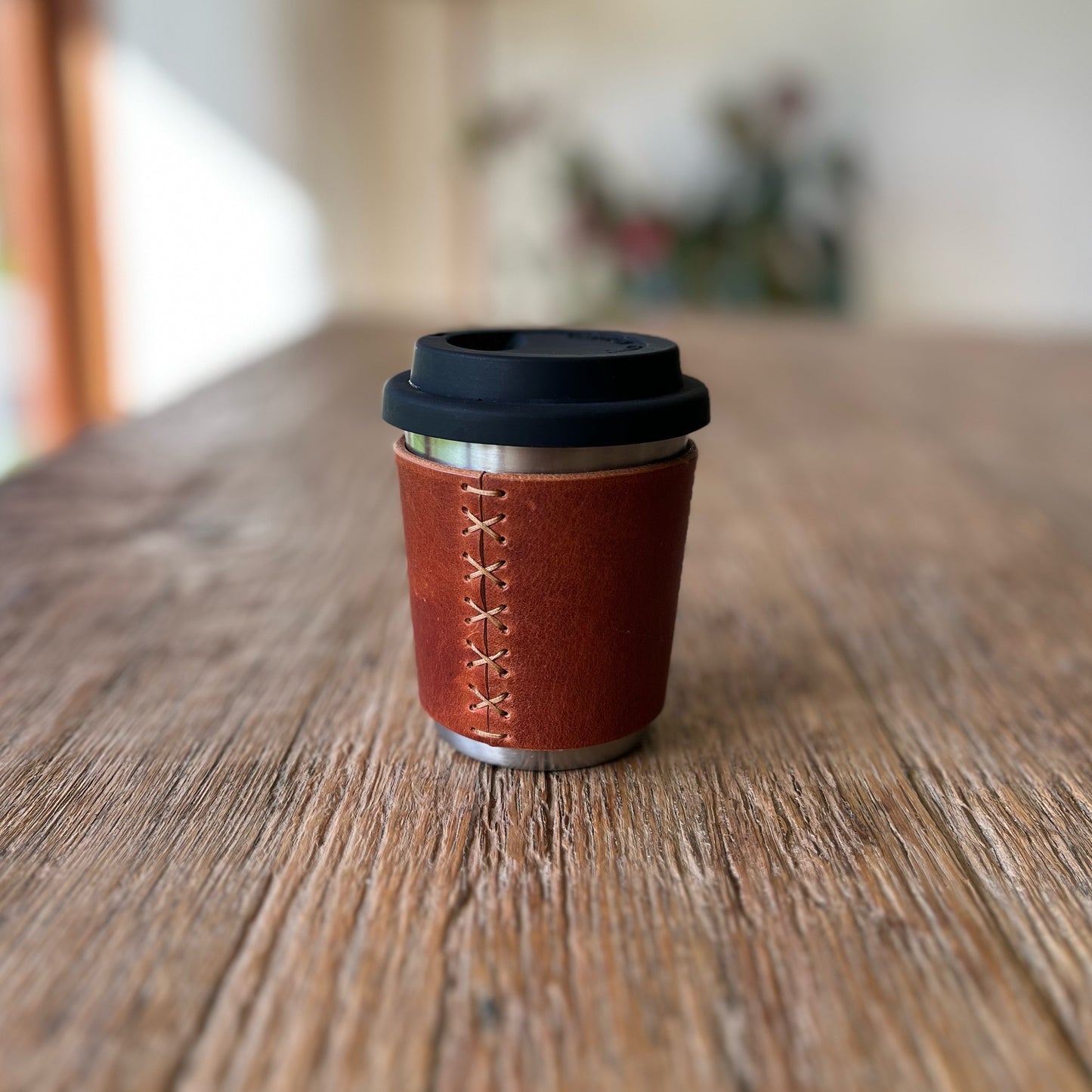Brown leather coffee cup with black lid on a wooden surface