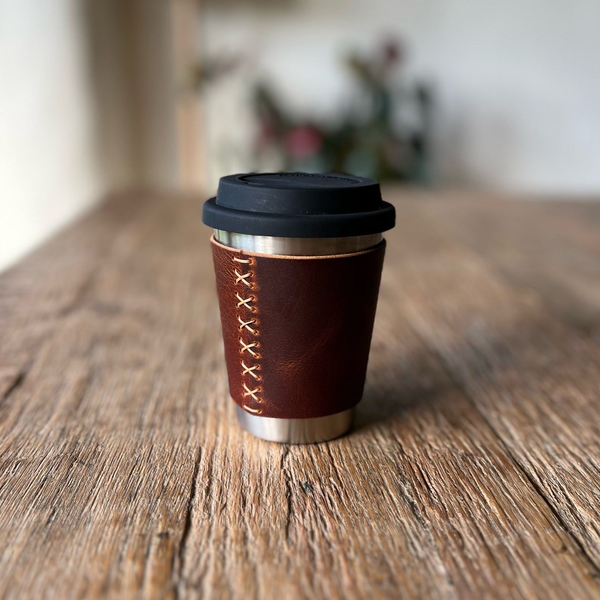 Dark brown leather travel mug with black lid on a wooden surface