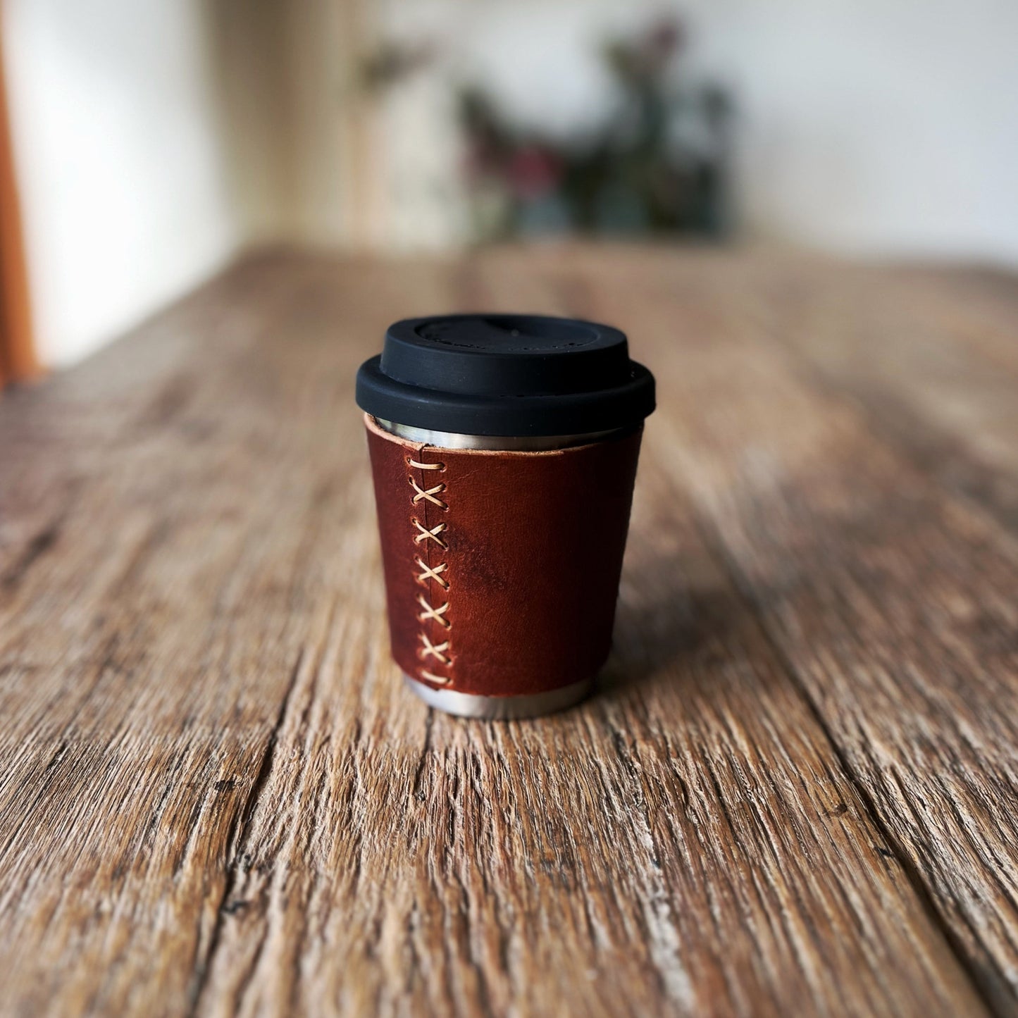 Travel coffee cup with brown leather sleeve and black lid on a wooden surface