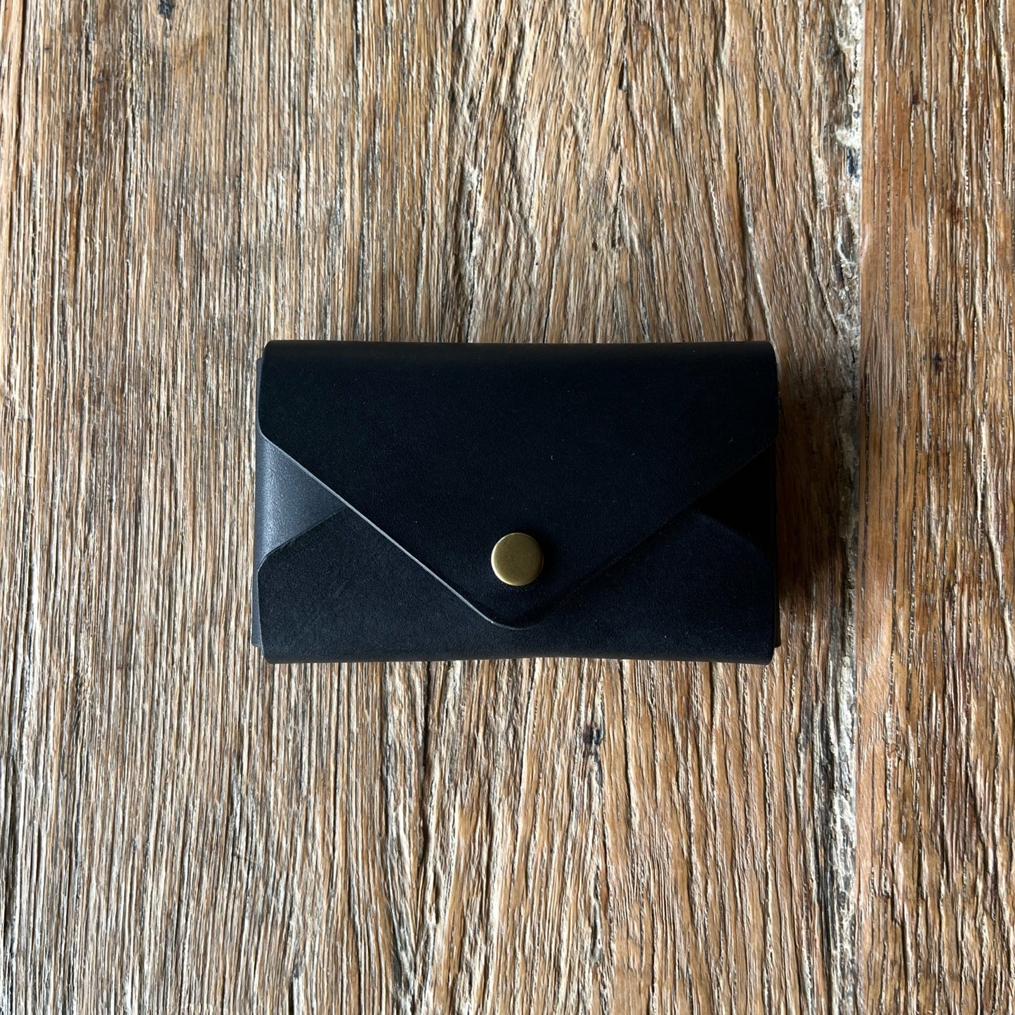 Black leather wallet with a brass snap button on a wooden surface