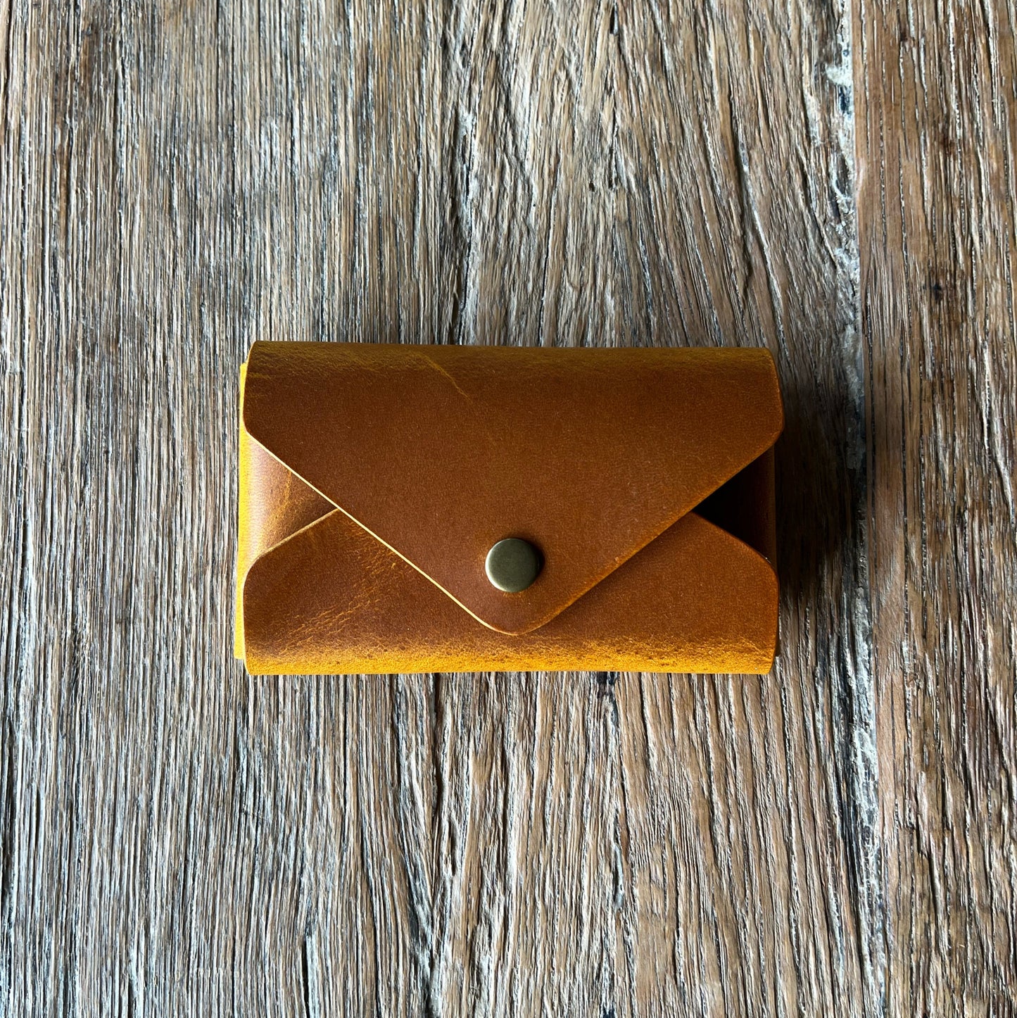 Tan leather wallet with a button on a wooden surface
