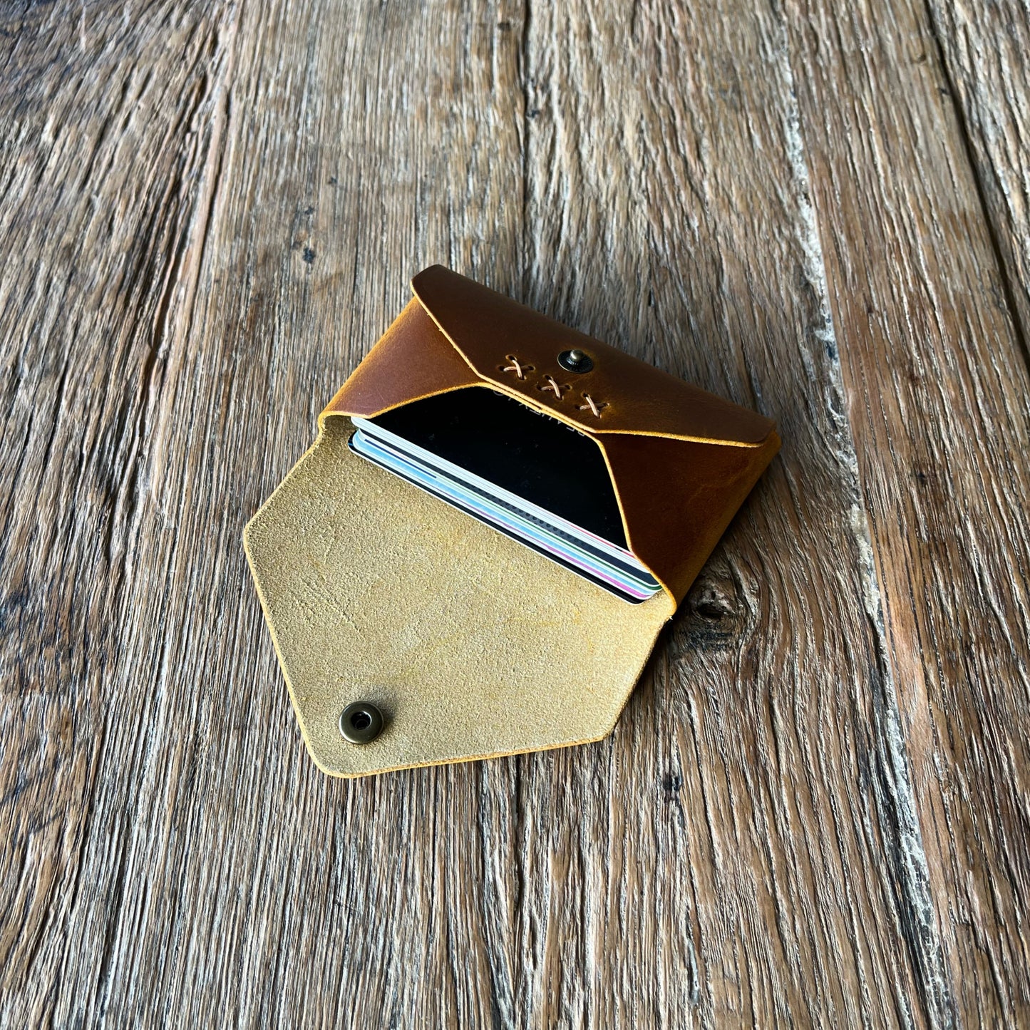 tan leather card holder with x-stitched detail holding stack of bank cards on a wooden surface