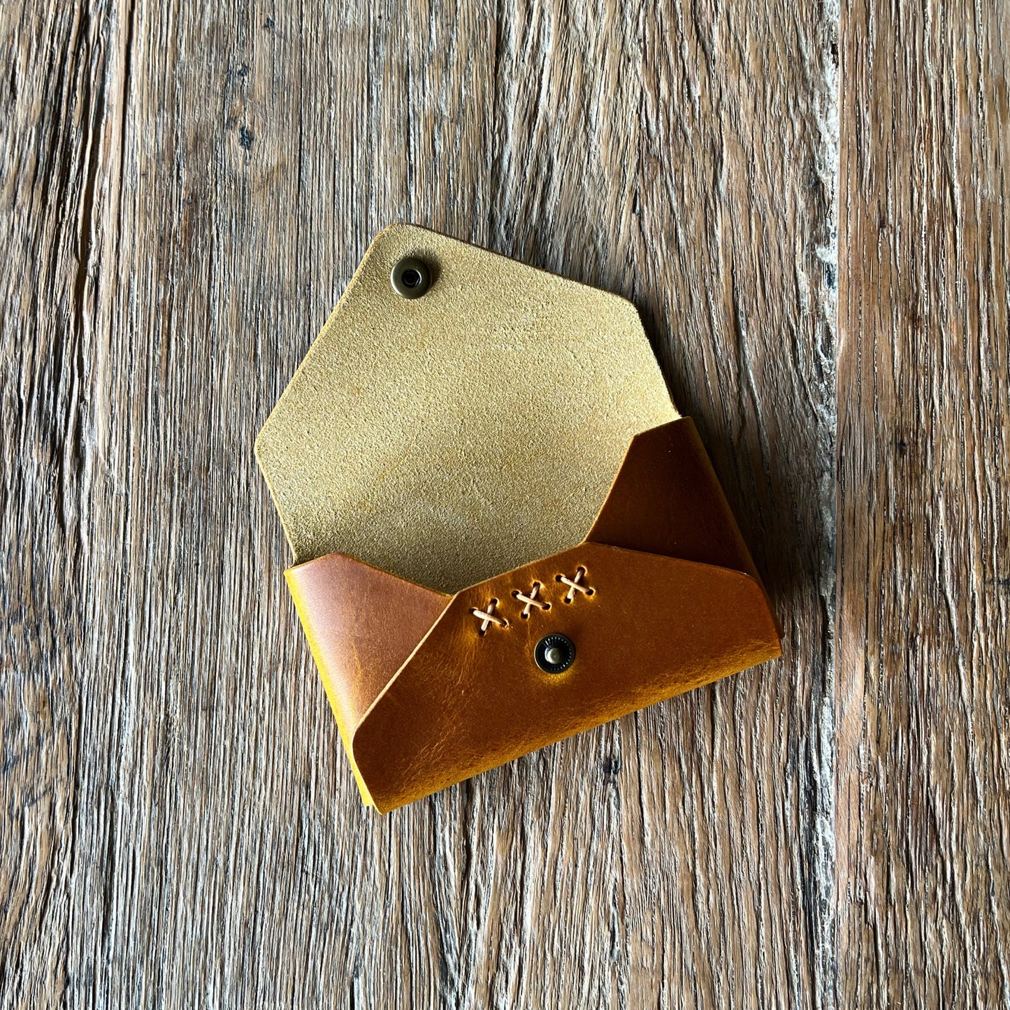 tan leather card holder with x-stitched detail on a wooden surface