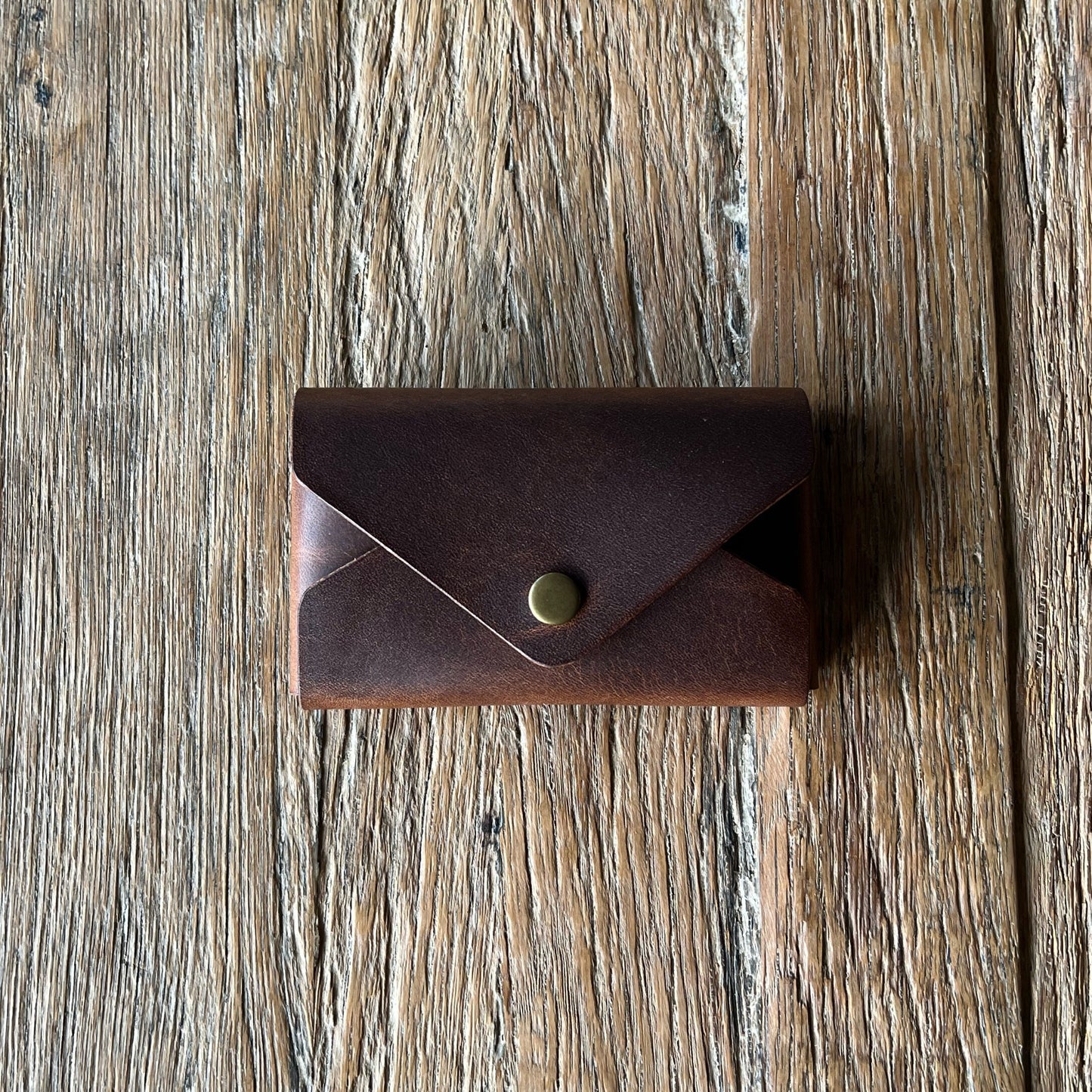 Brown leather wallet with a brass snap button on a wooden surface