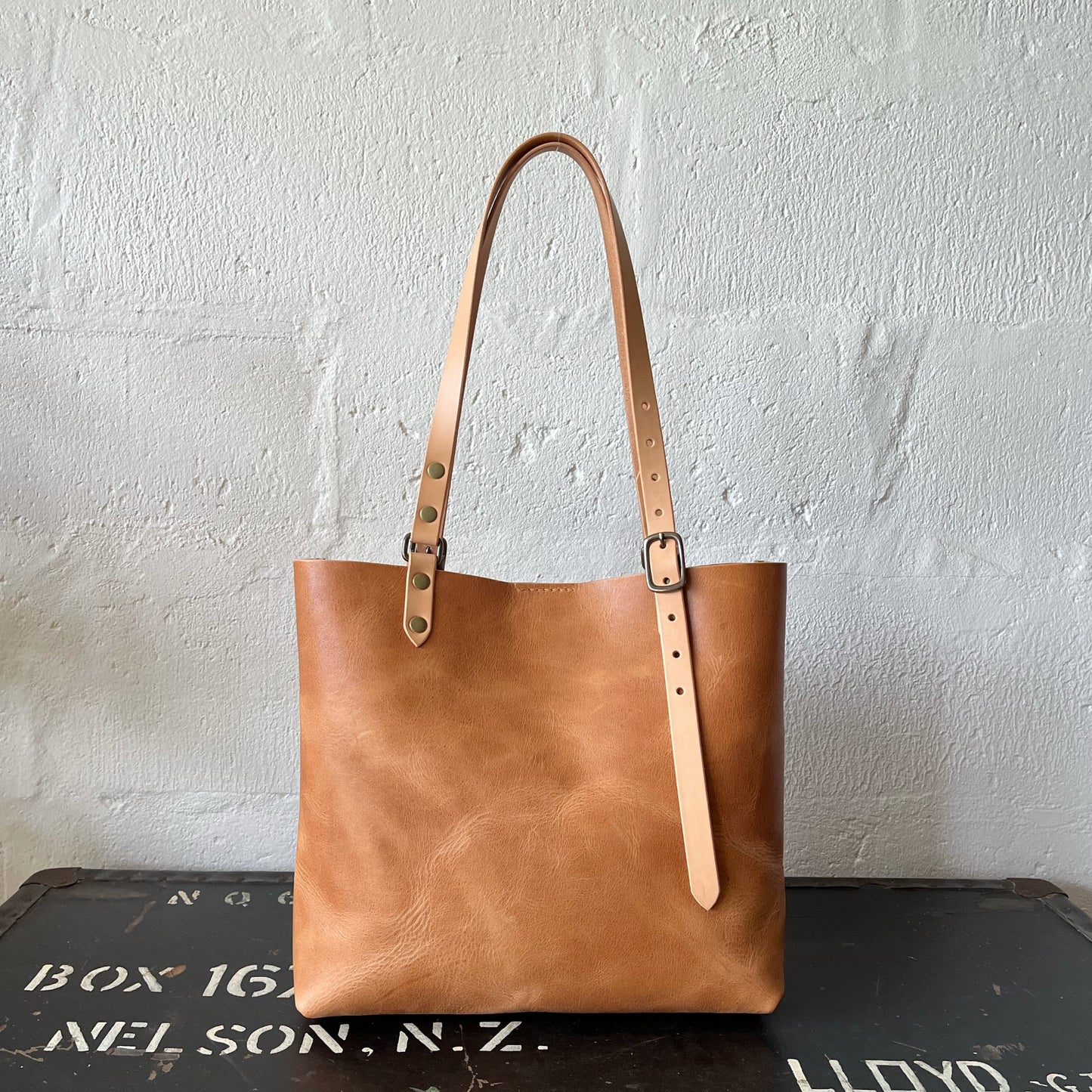 Brown leather tote bag with strap on a textured surface