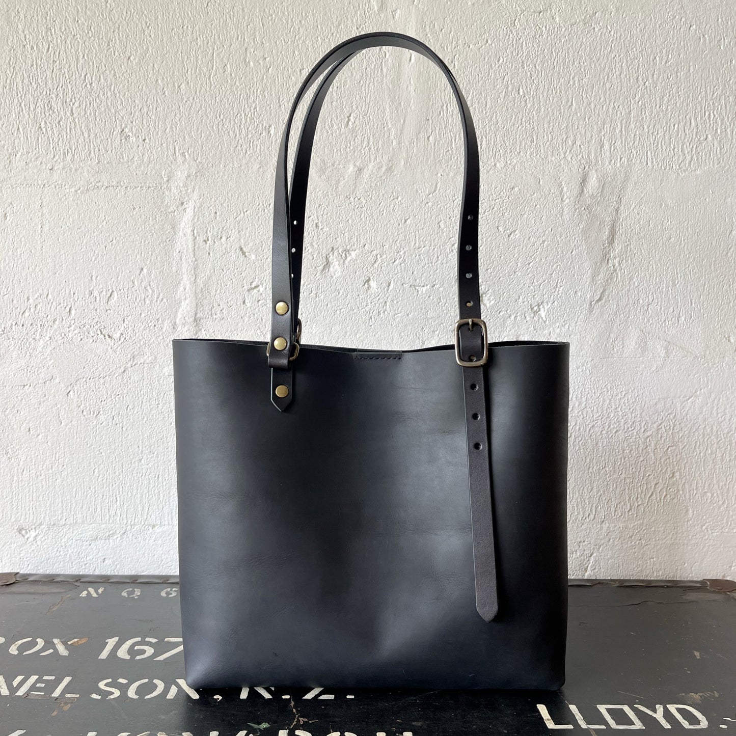 Black leather tote bag with a strap on a textured surface