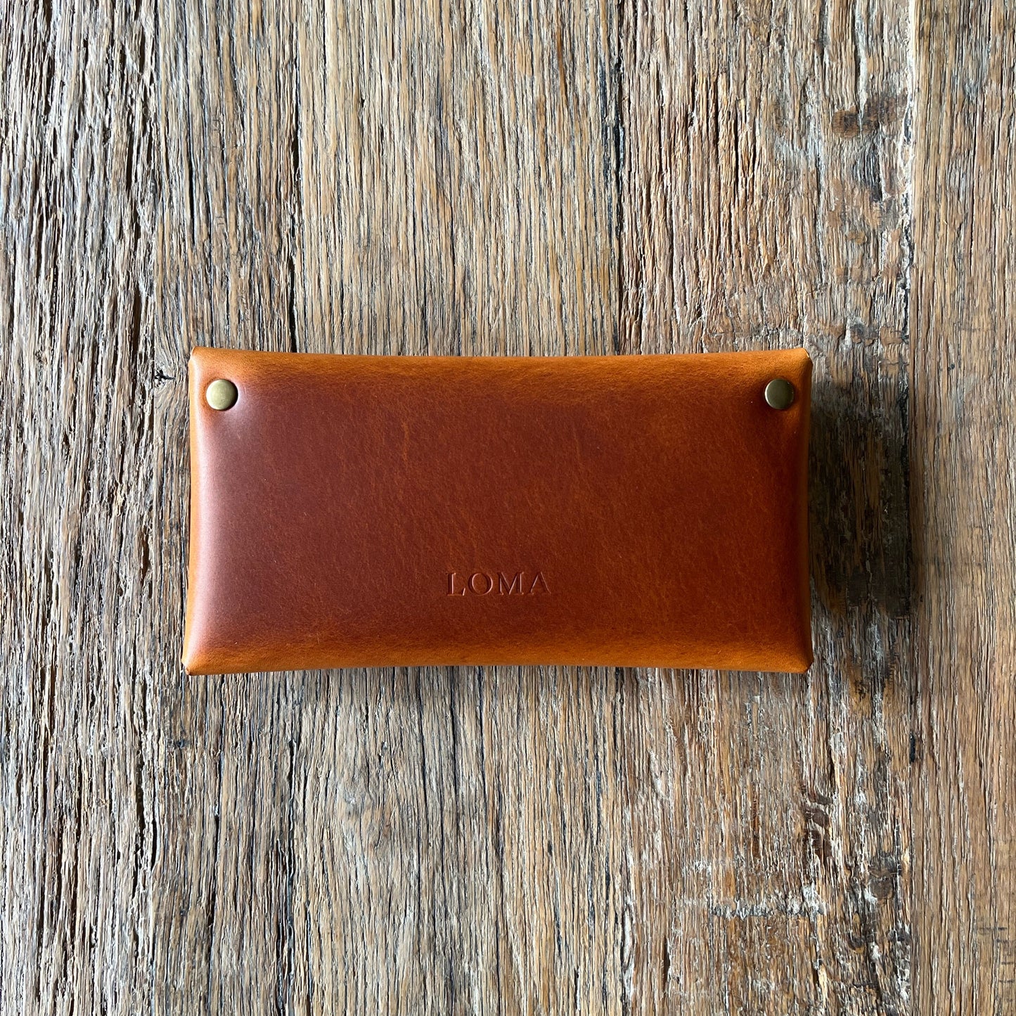 Brown leather pouch with 'LOMA' branding on a wooden surface