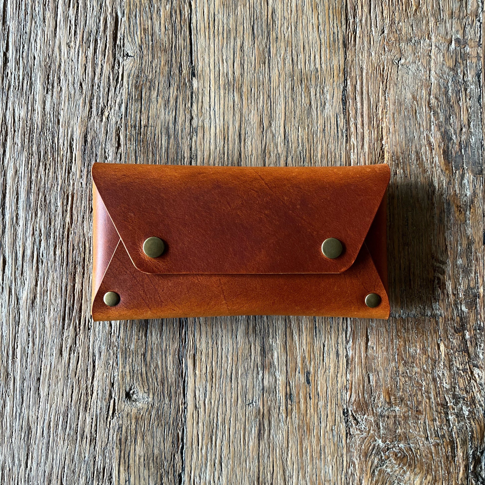 Brown leather wallet with brass  rivets on a wooden surface