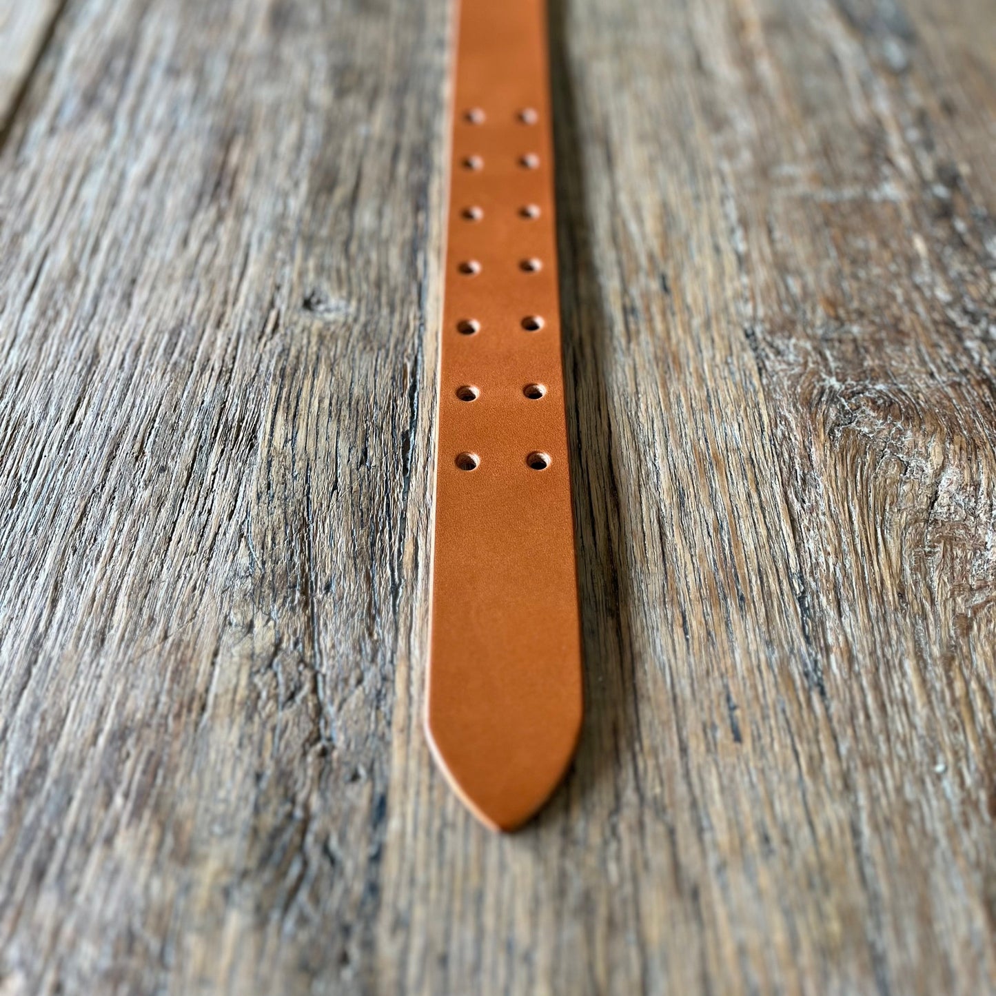 Tan leather belt with double prong brass buckle end detail