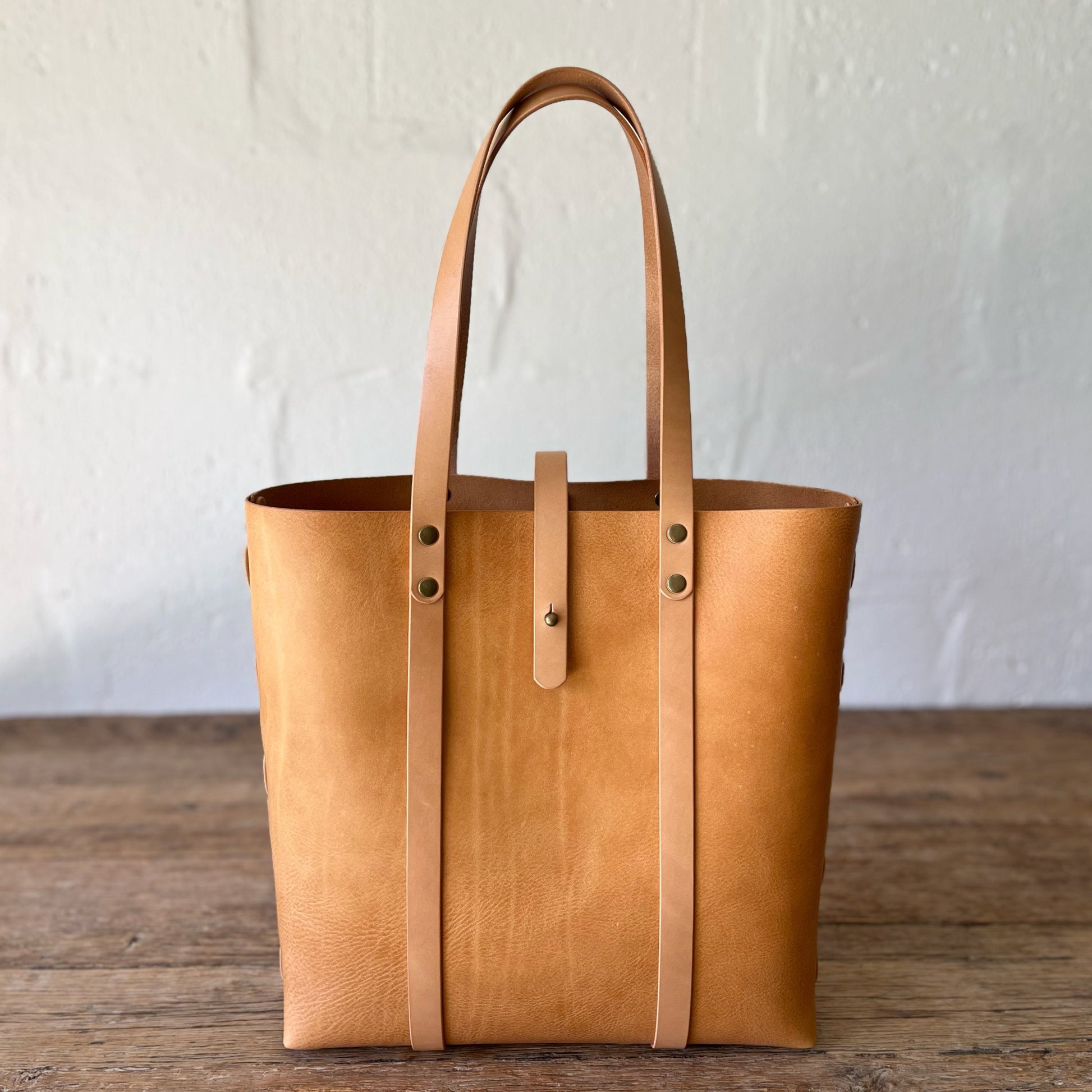 Brown leather tote bag on a wooden surface with a white background
