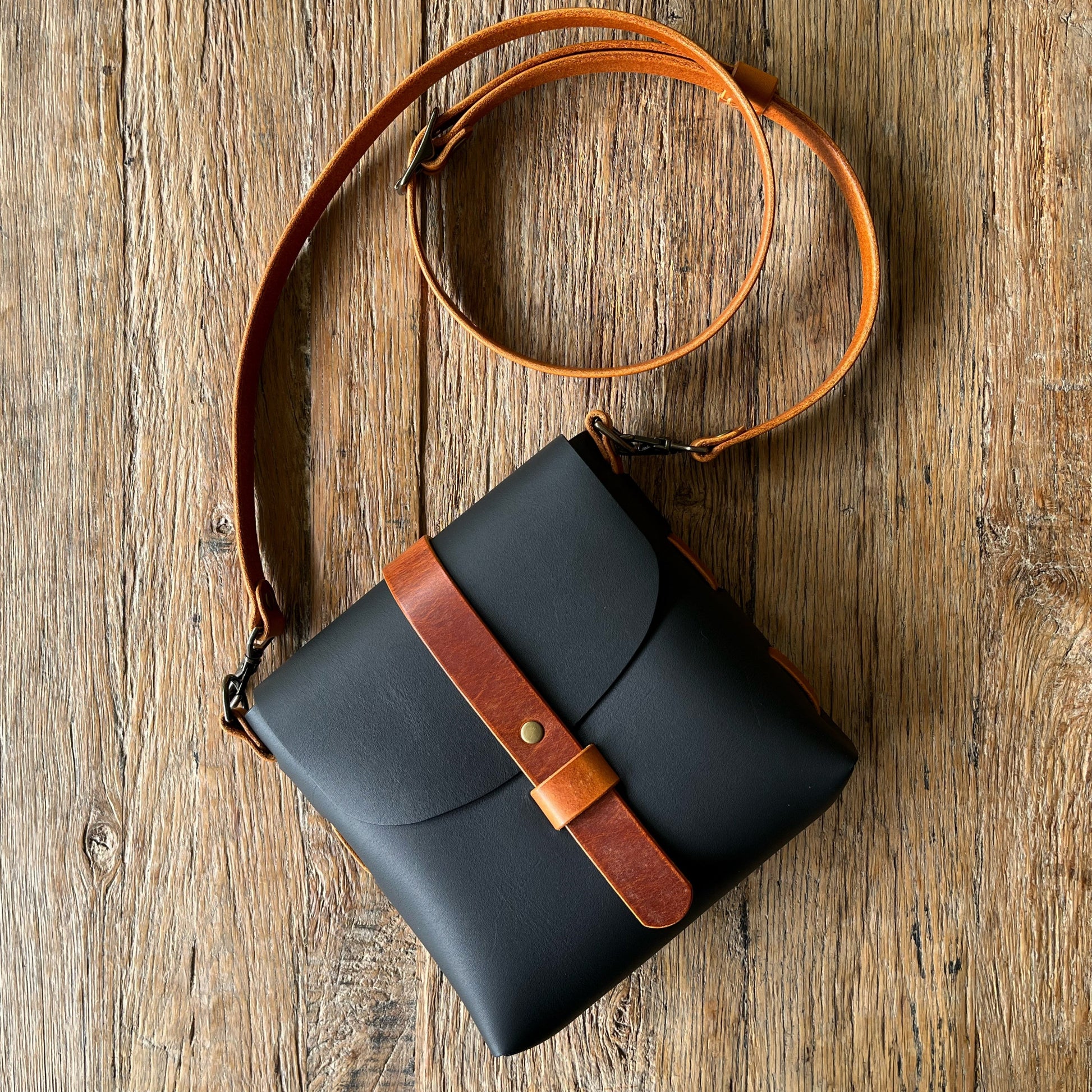 Black leather crossbody bag with brown strap on a wooden surface