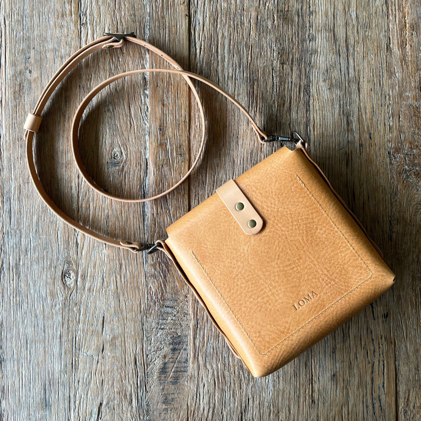 Tan leather crossbody bag on a wooden surface
