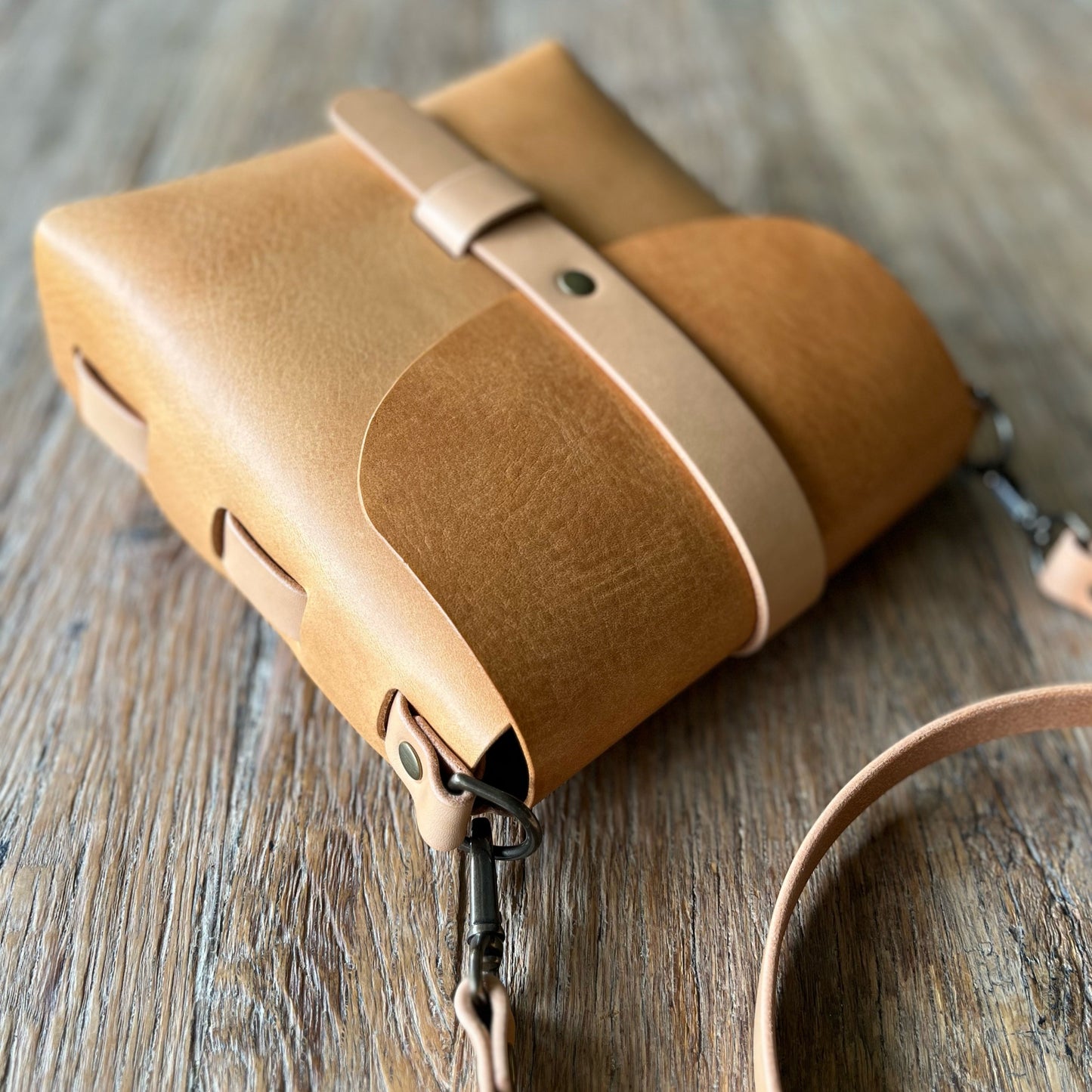 Tan leather bag with strap on a wooden surface