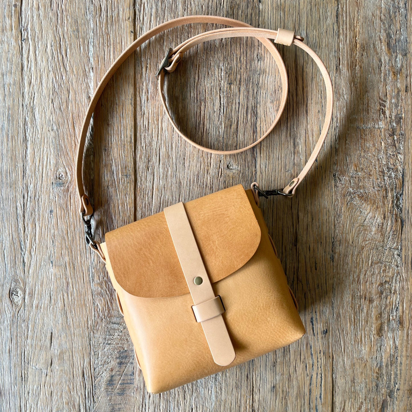 Tan leather crossbody bag on a wooden surface