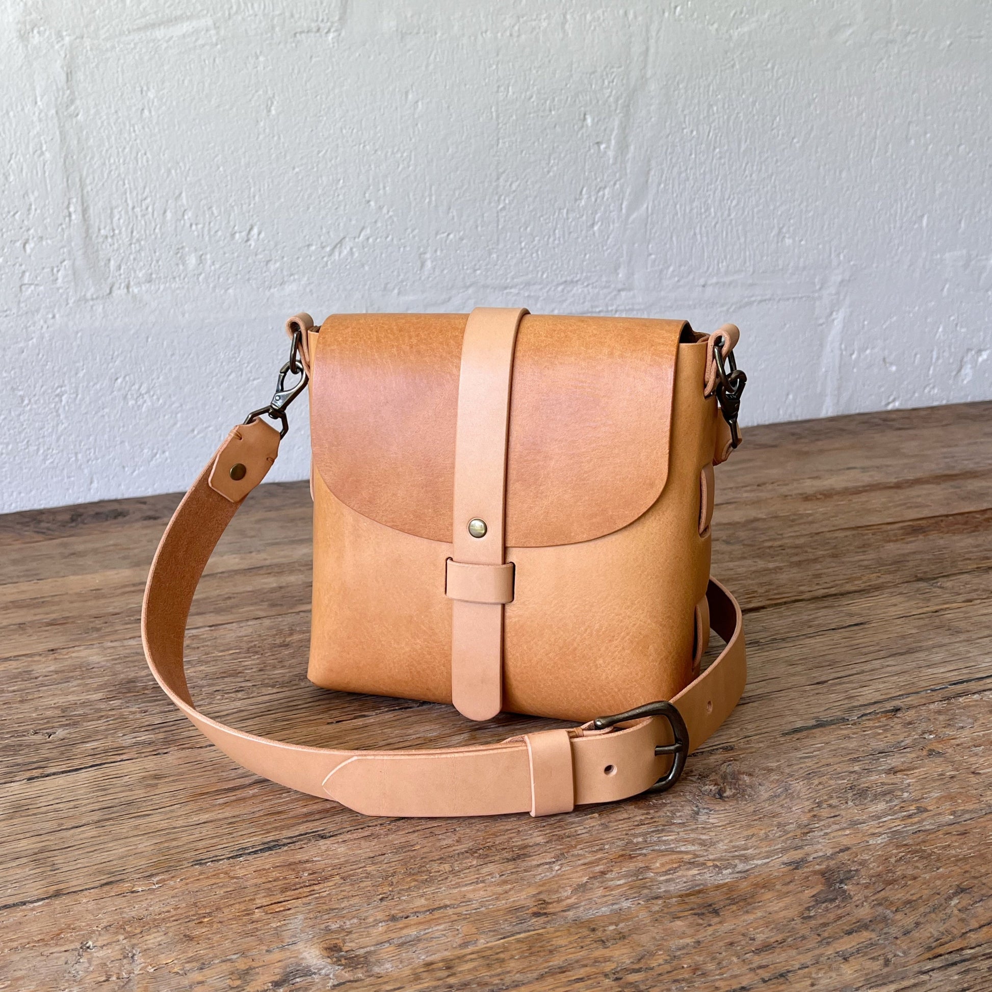 Tan leather bag on a wooden surface with a white textured wall background