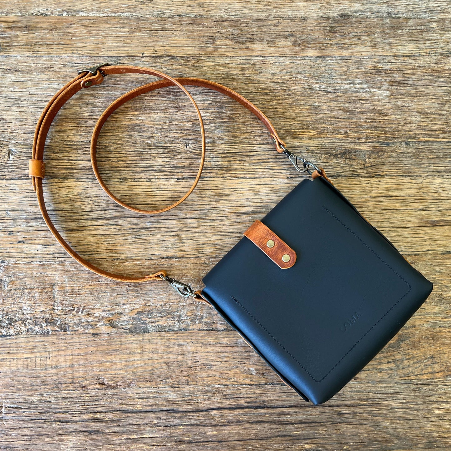 Black crossbody bag with brown strap on a wooden surface