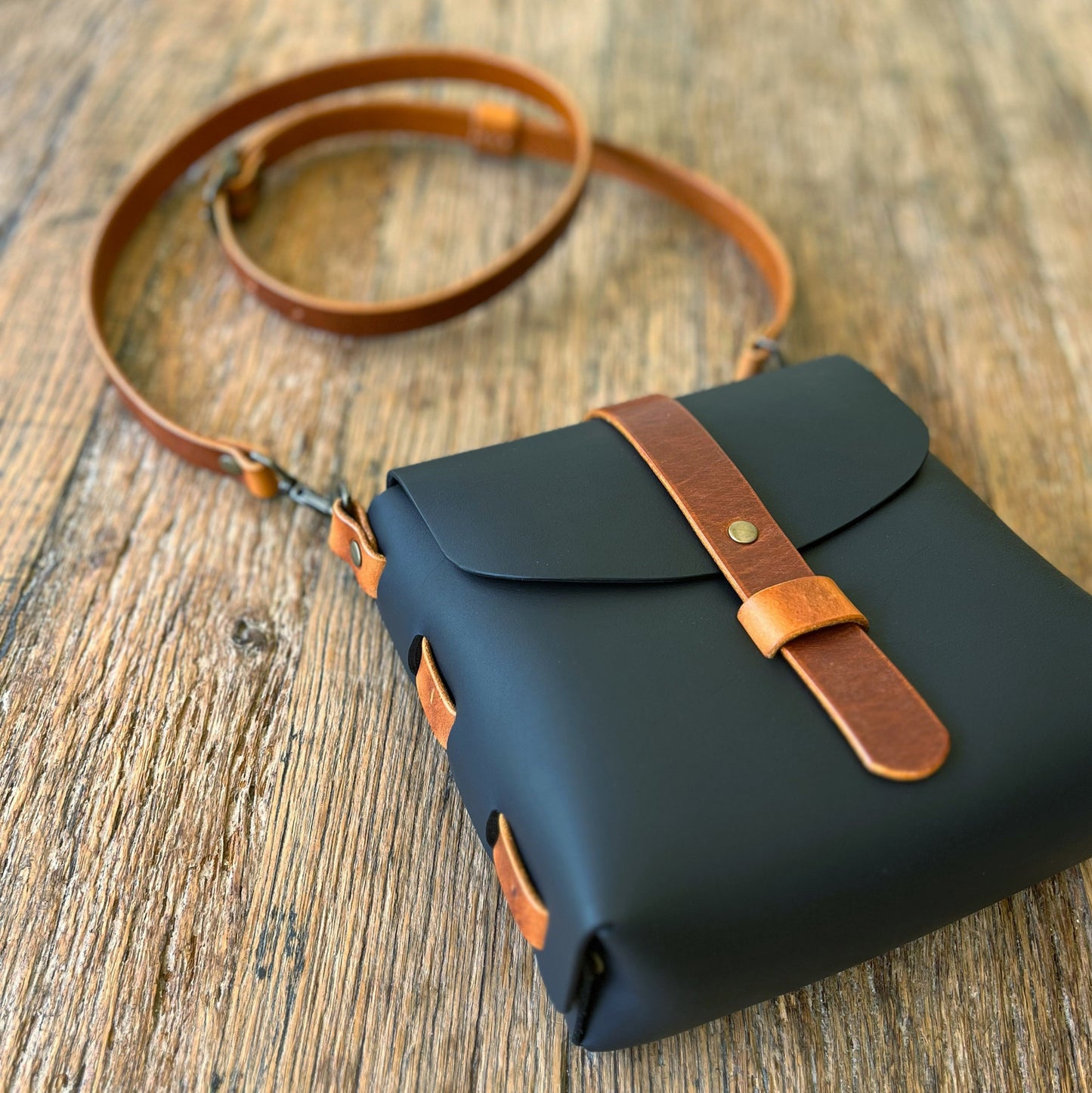 Black bag with brown leather strap on a wooden surface
