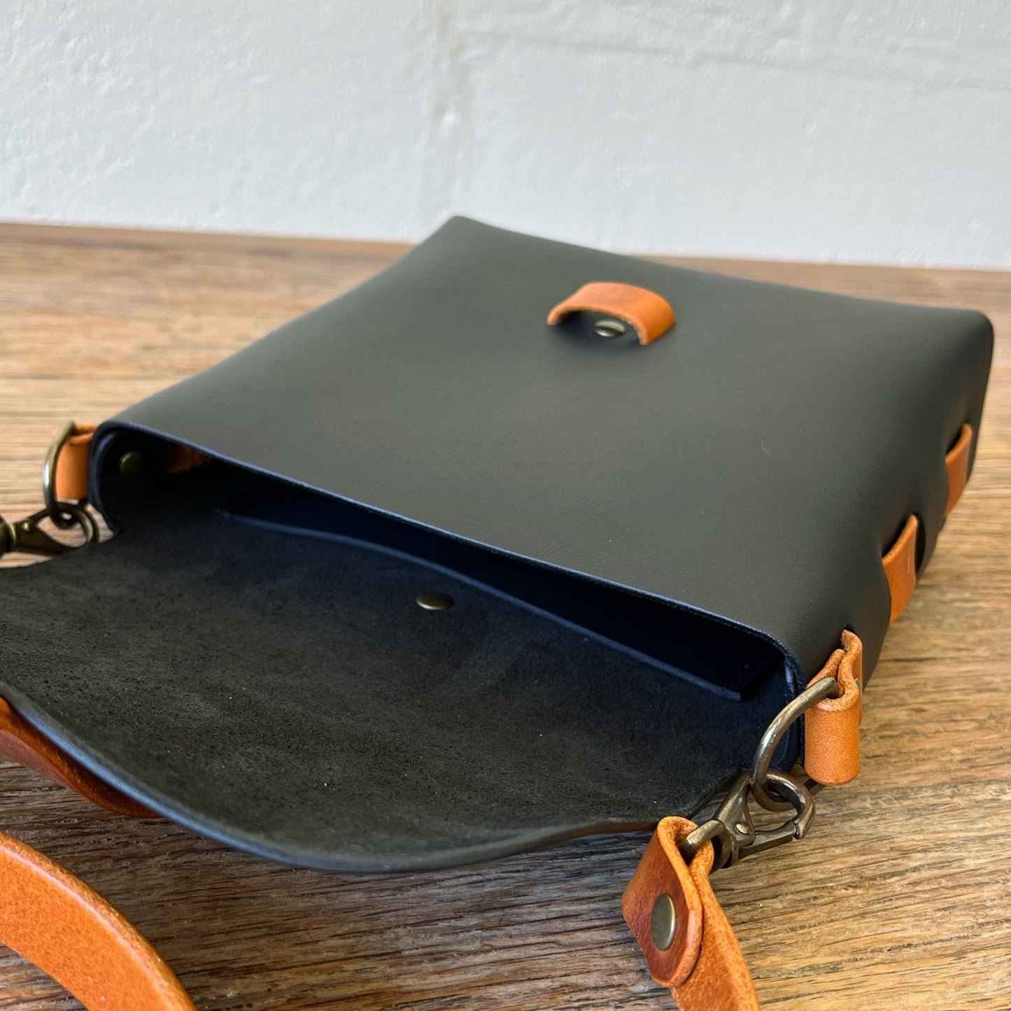 Black leather bag with brown accents on a wooden surface