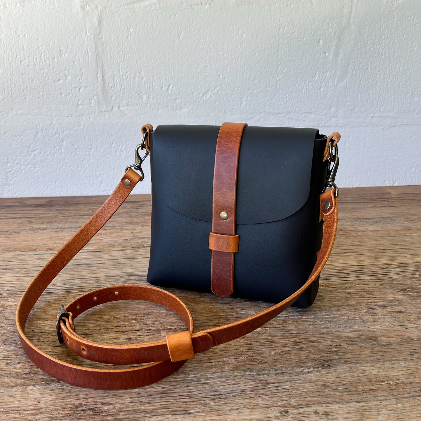 Black leather bag with brown strap on a wooden surface