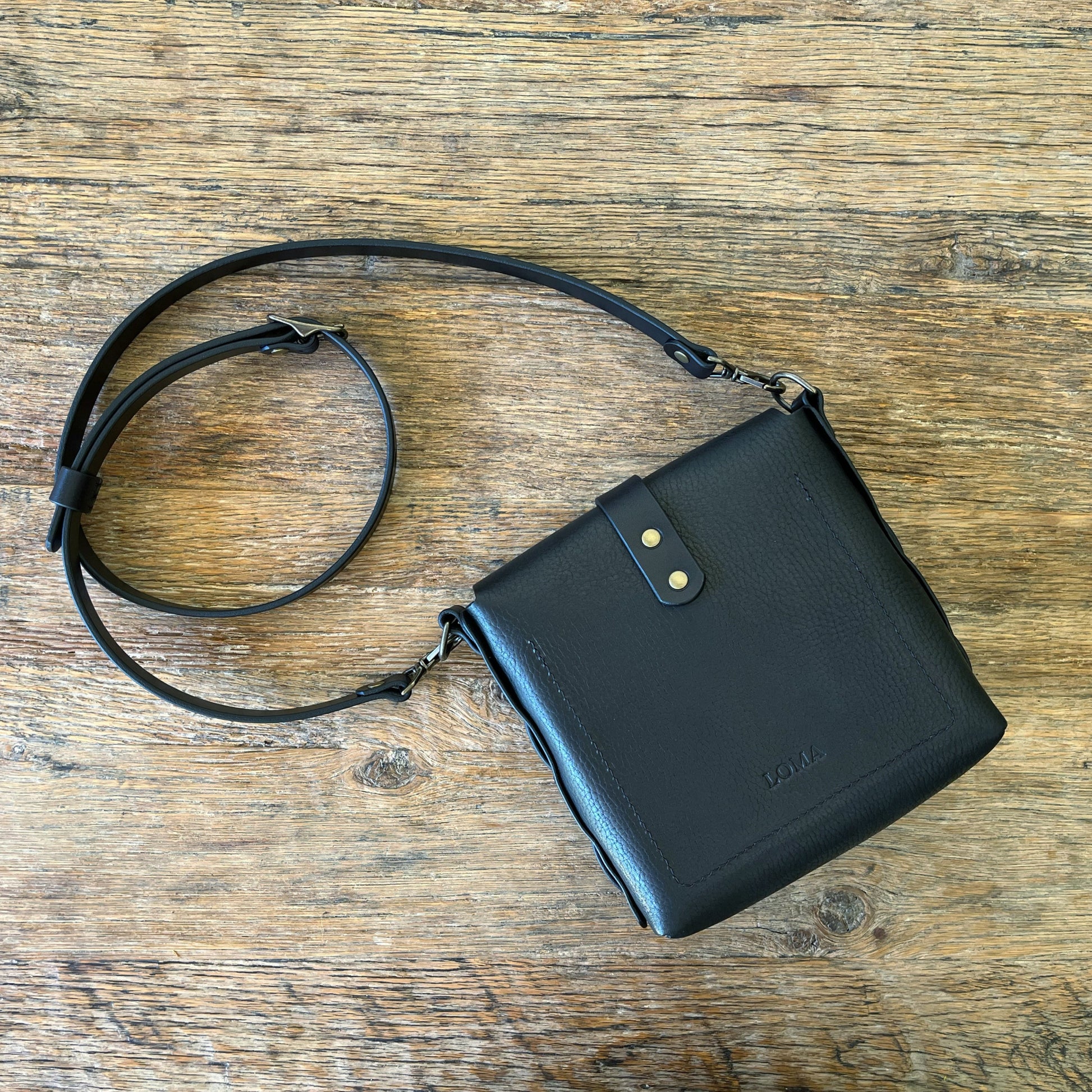 Black leather crossbody bag on a wooden surface