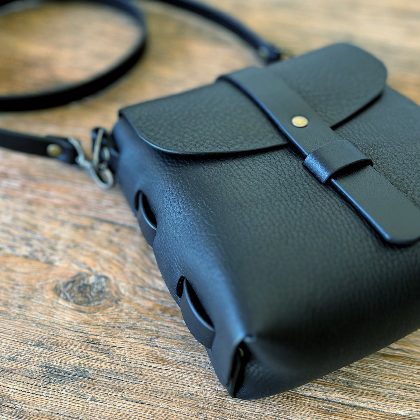 Black leather bag with a strap on a wooden surface