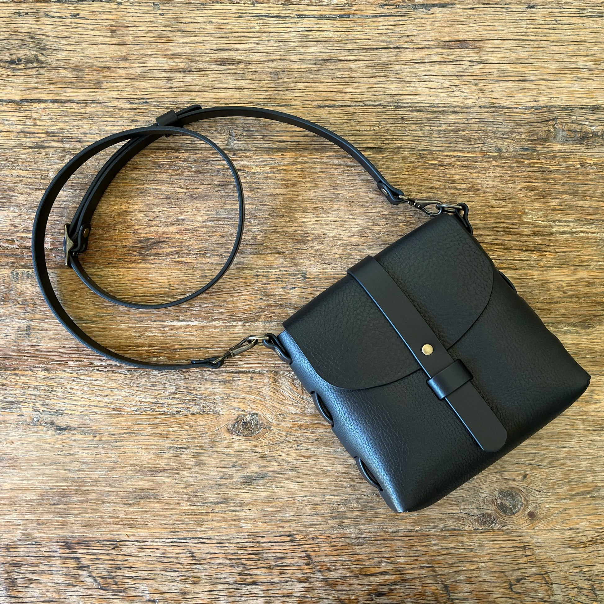 Black leather handbag with a strap on a wooden surface