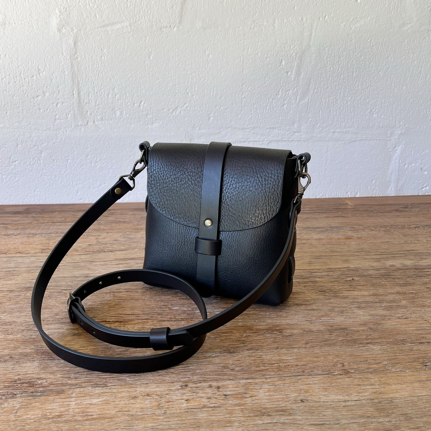 Black leather handbag with a strap on a wooden surface against a white wall