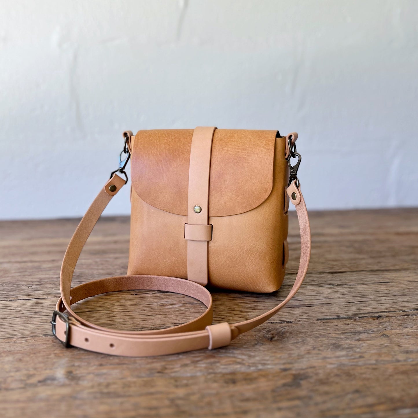 Tan leather crossbody bag on a wooden surface with a white background