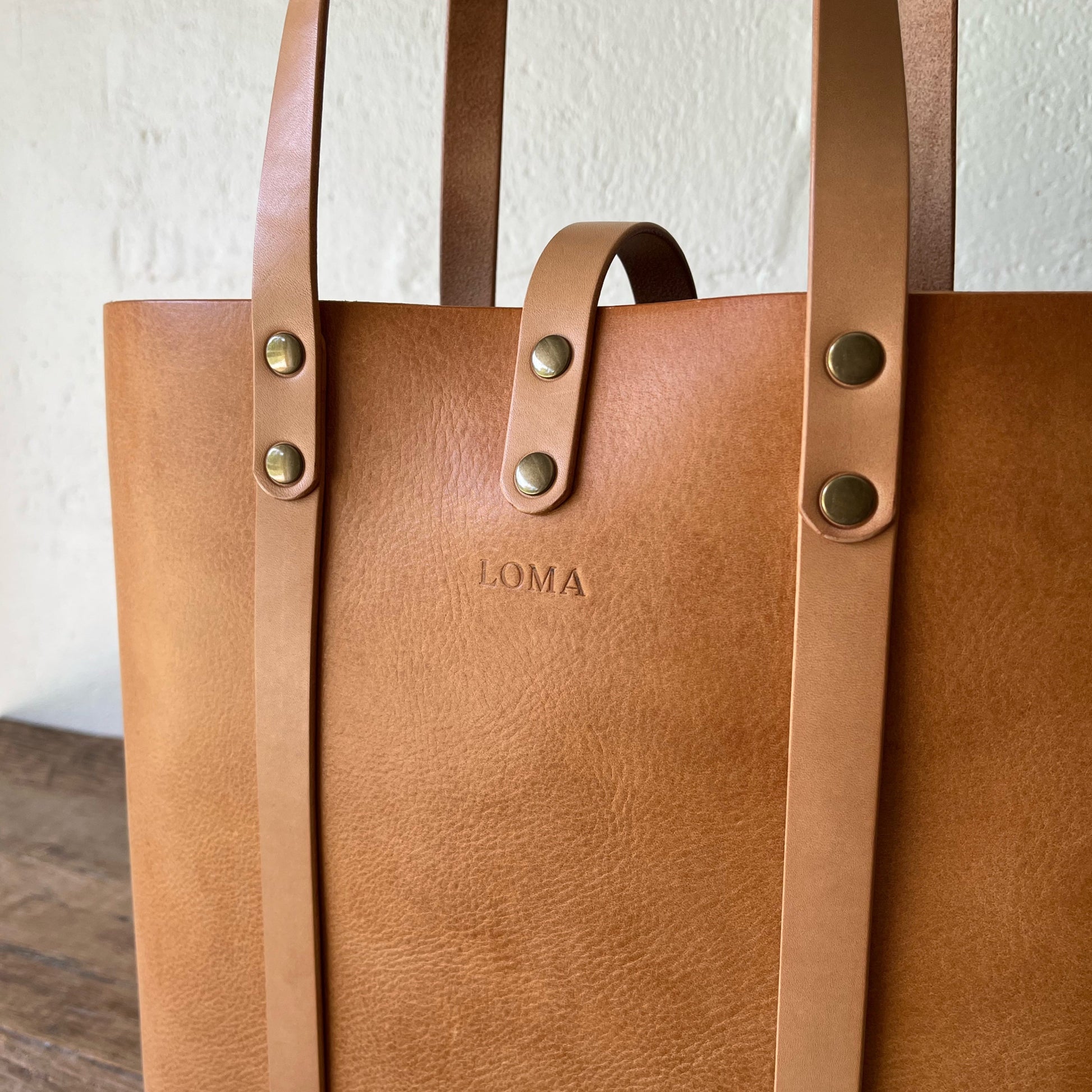 Tan leather tote bag with 'LOMA' branding on a light background