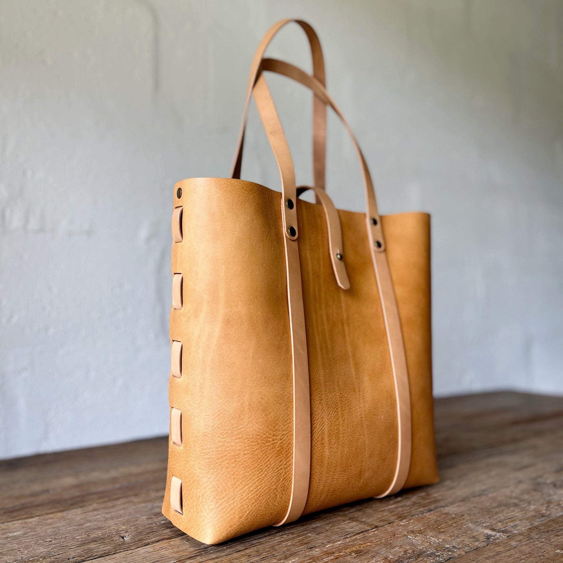 Tan leather tote bag with strap on a wooden surface