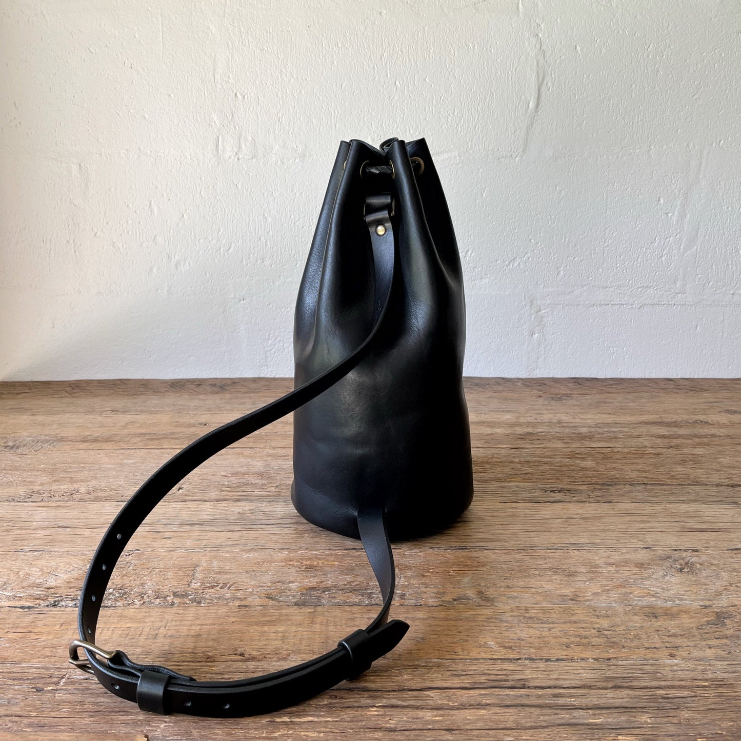 Black leather bucket bag on a wooden surface with a white wall background