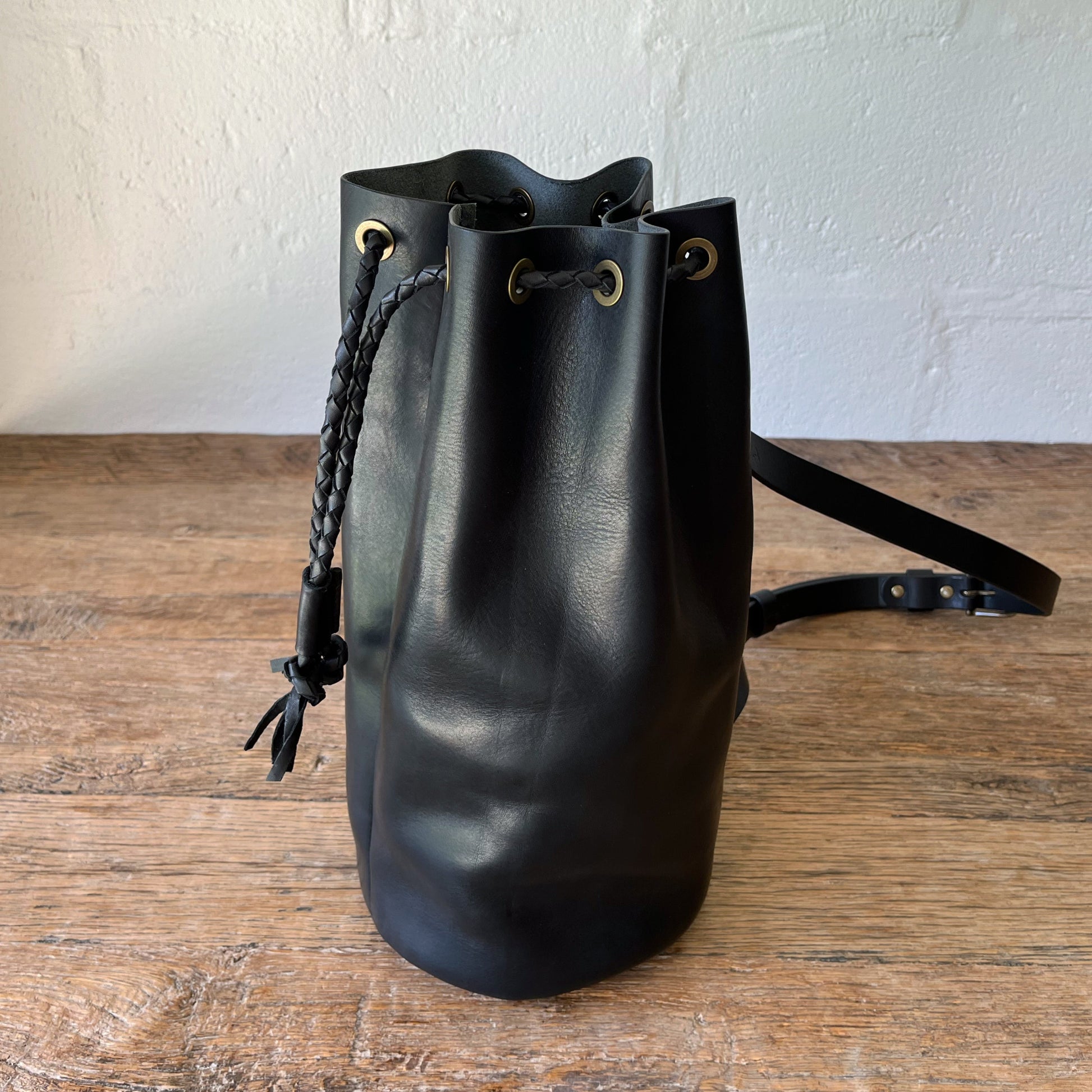 Black leather duffle bag on a wooden surface with a white wall background