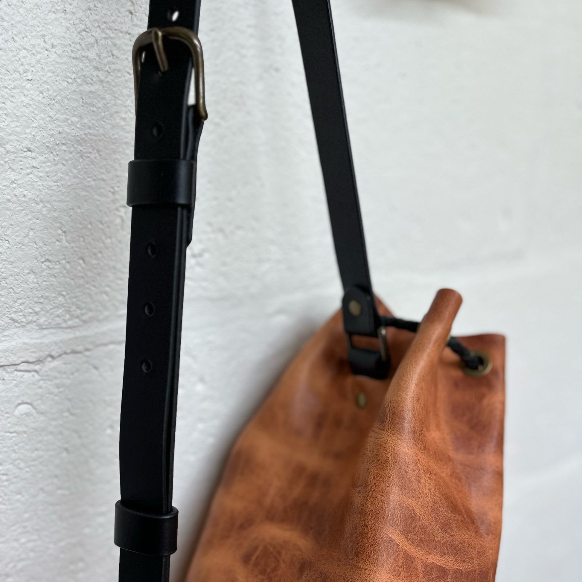 Brown leather bag with black strap on a white background