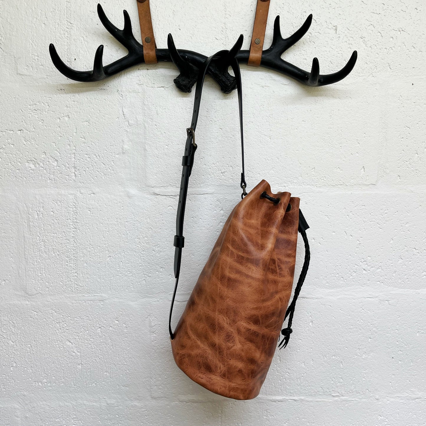 Brown leather drawstring bag hanging on a wall hook with antlers.