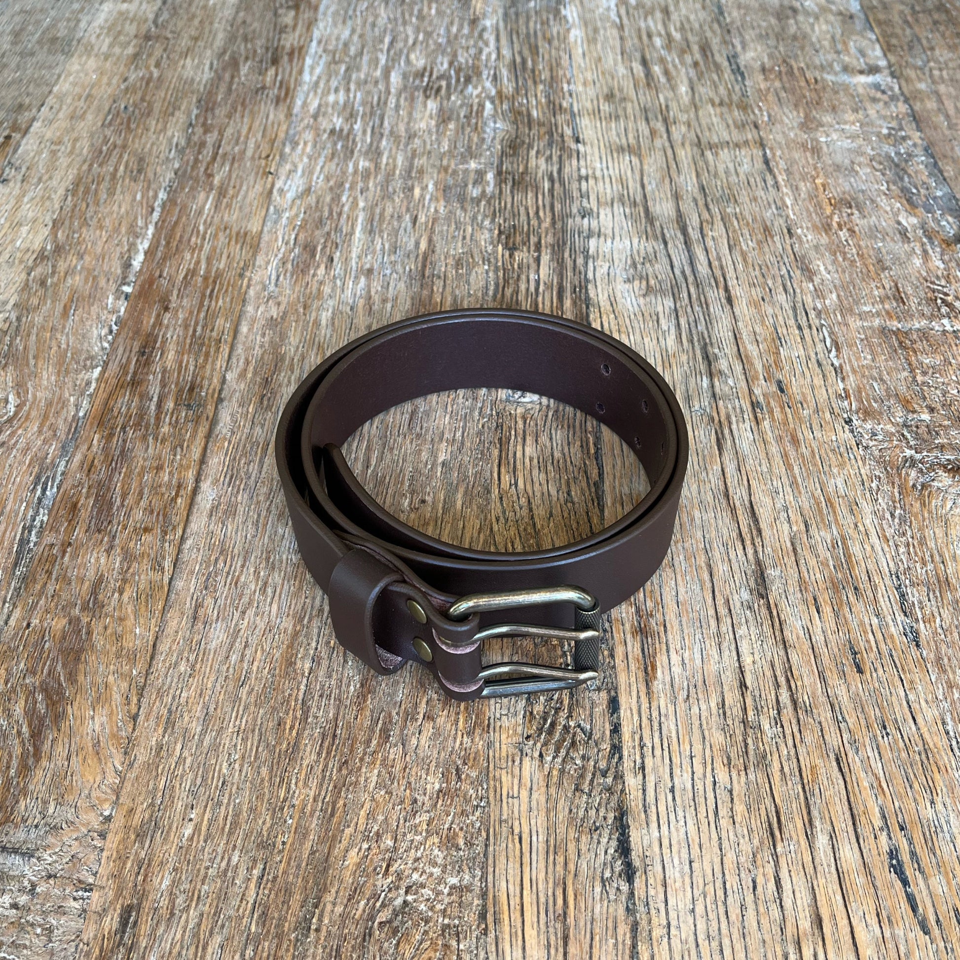 Brown leather belt with antique finish solid brass buckle on a wooden surface