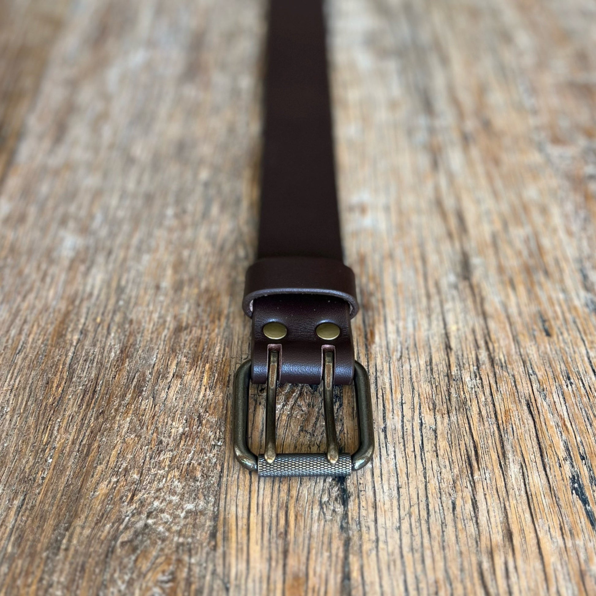 Brown leather belt with brass buckle on a wooden surface