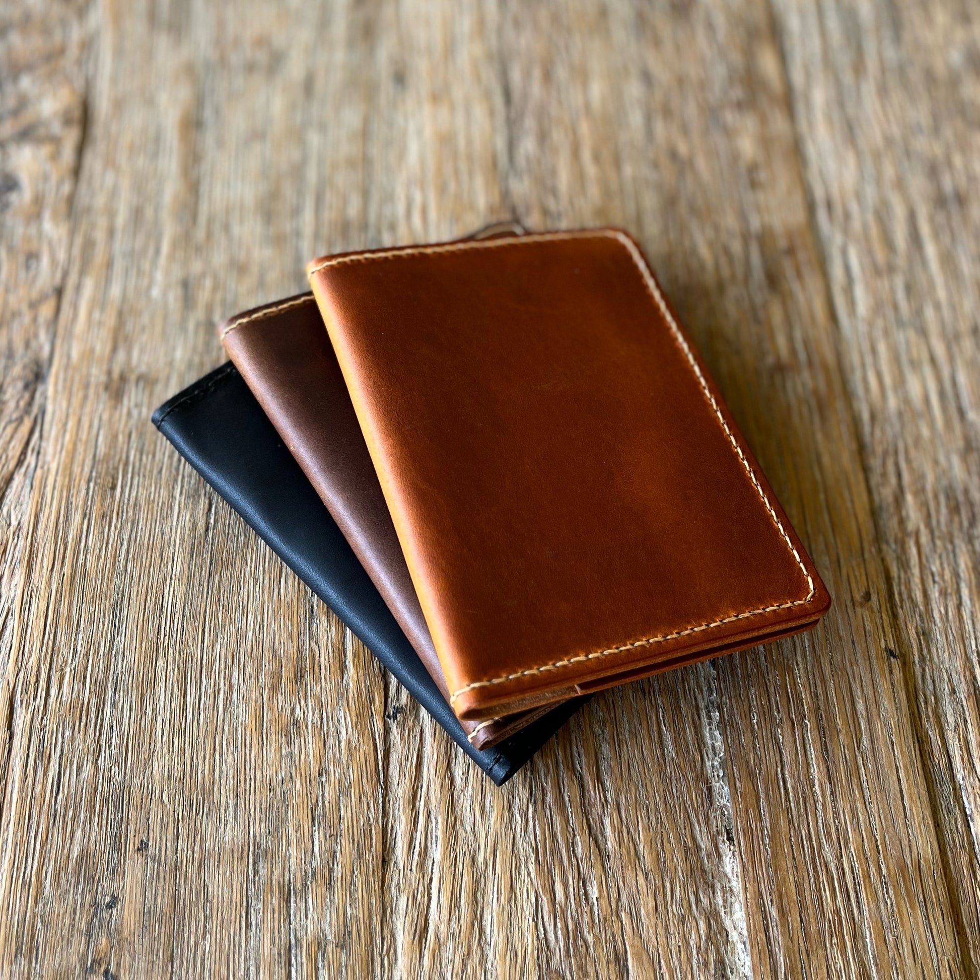 leather passport covers lying on a wooden surface, one in black and one in brown and one tan