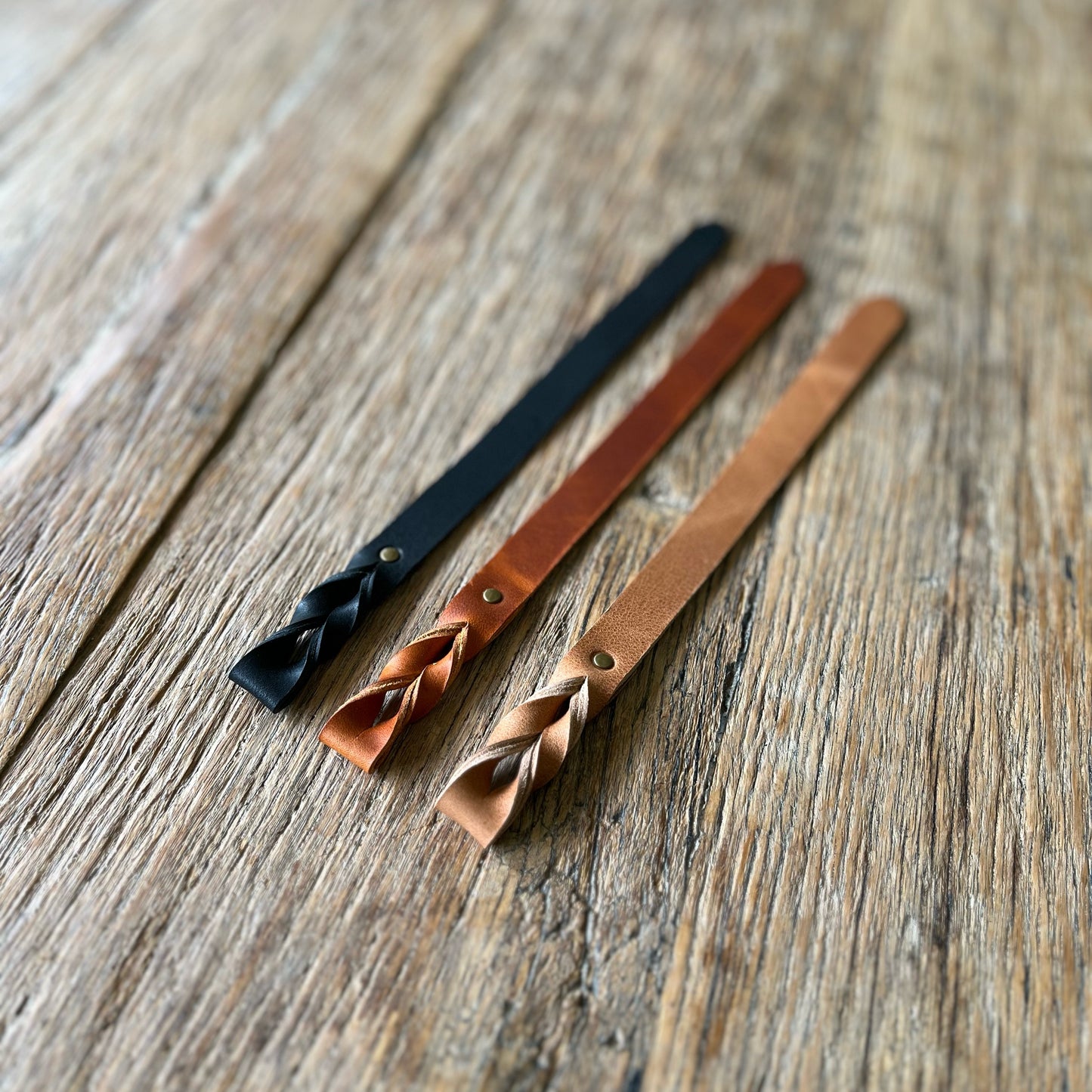 Three leather bookmarks with braided ends on a wooden surface