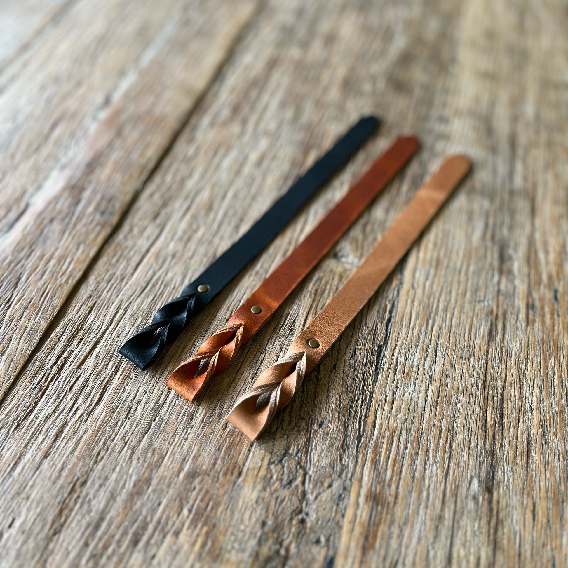 Three leather bookmarks with braided ends on a wooden surface