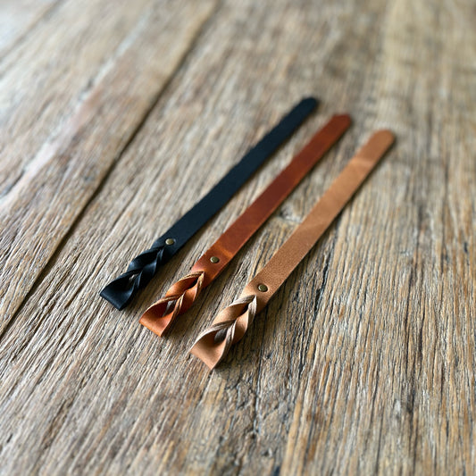 Three leather bookmarks with braided ends on a wooden surface