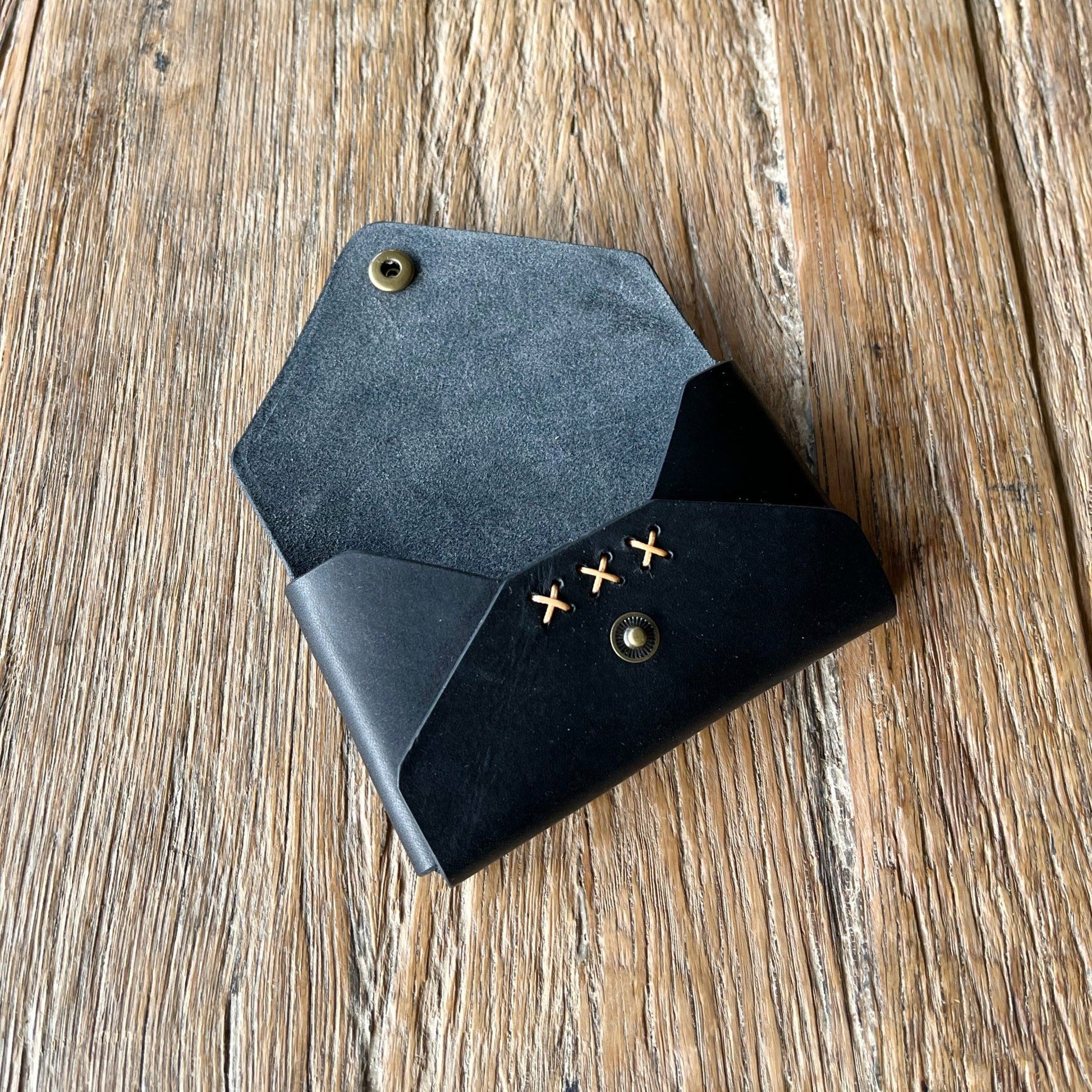 Black leather wallet with contrasting x-stitched detail on a wooden surface