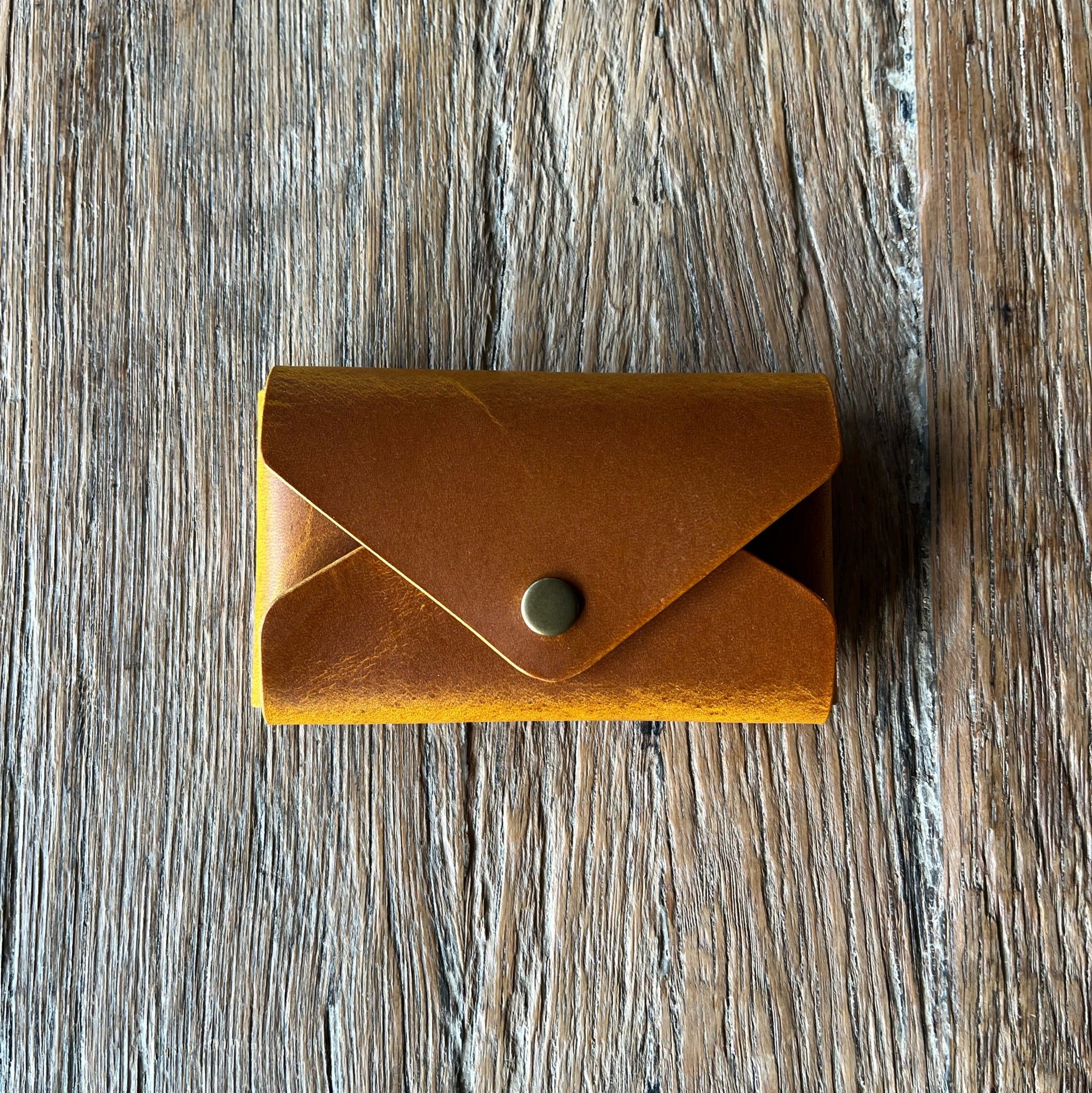 Tan leather wallet with a button on a wooden surface