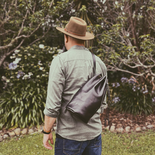 Man wearing a hat and carrying a black bag in a garden setting