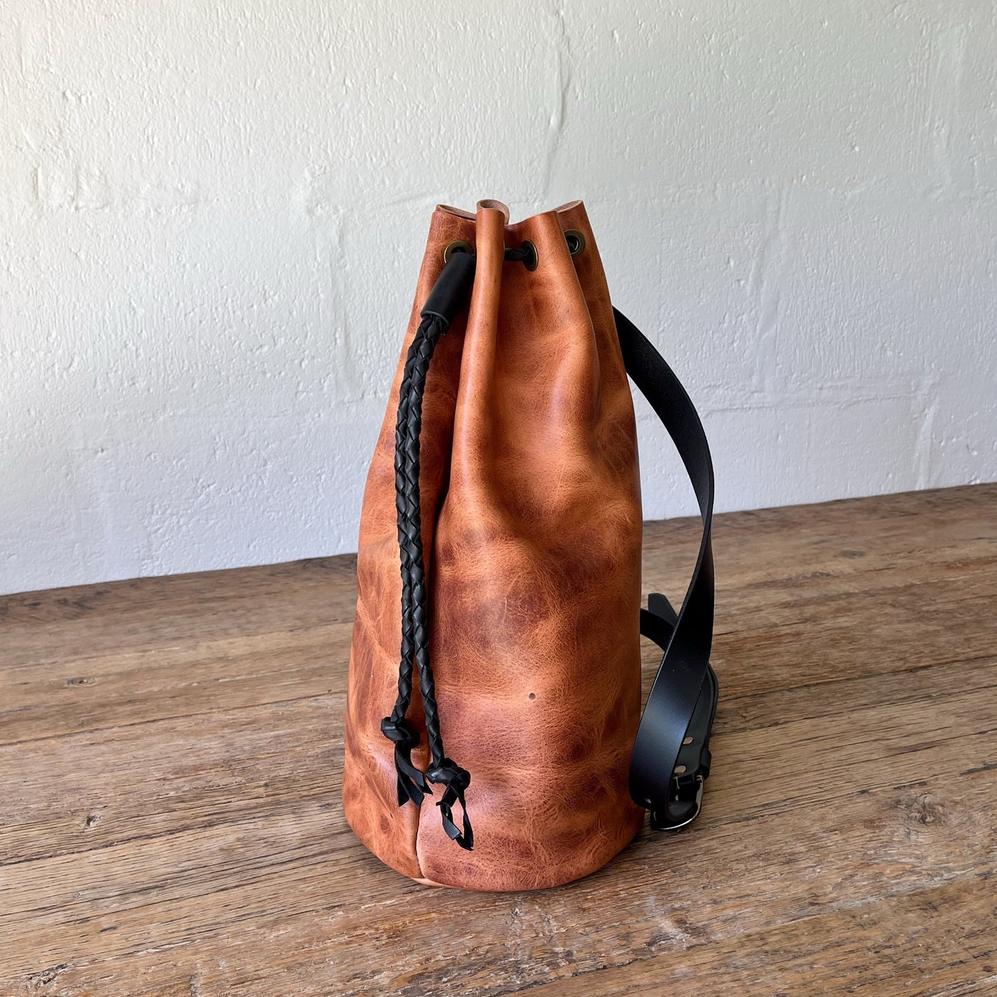 Brown leather backpack with black drawstring on a wooden surface